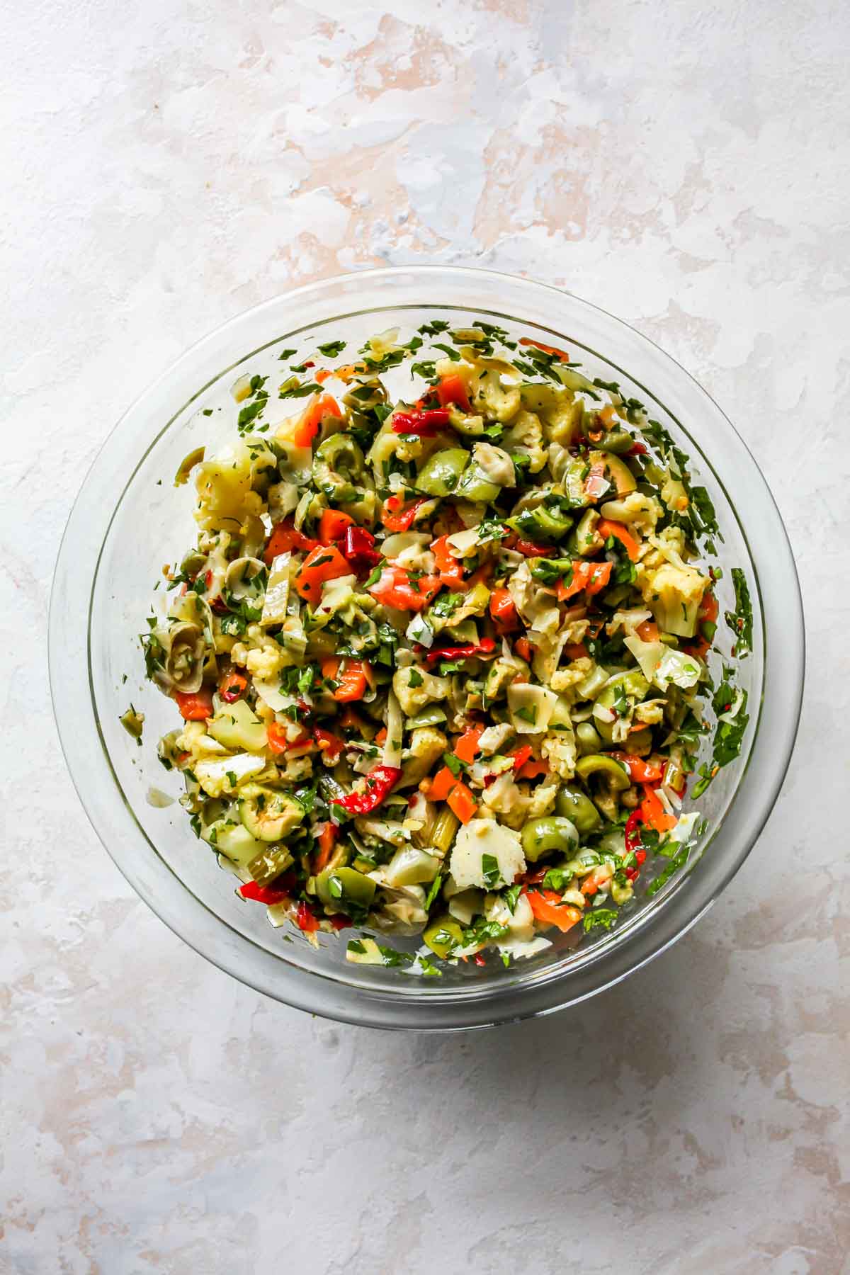 Artichoke salad being mixed until combined in a clear mixing bowl