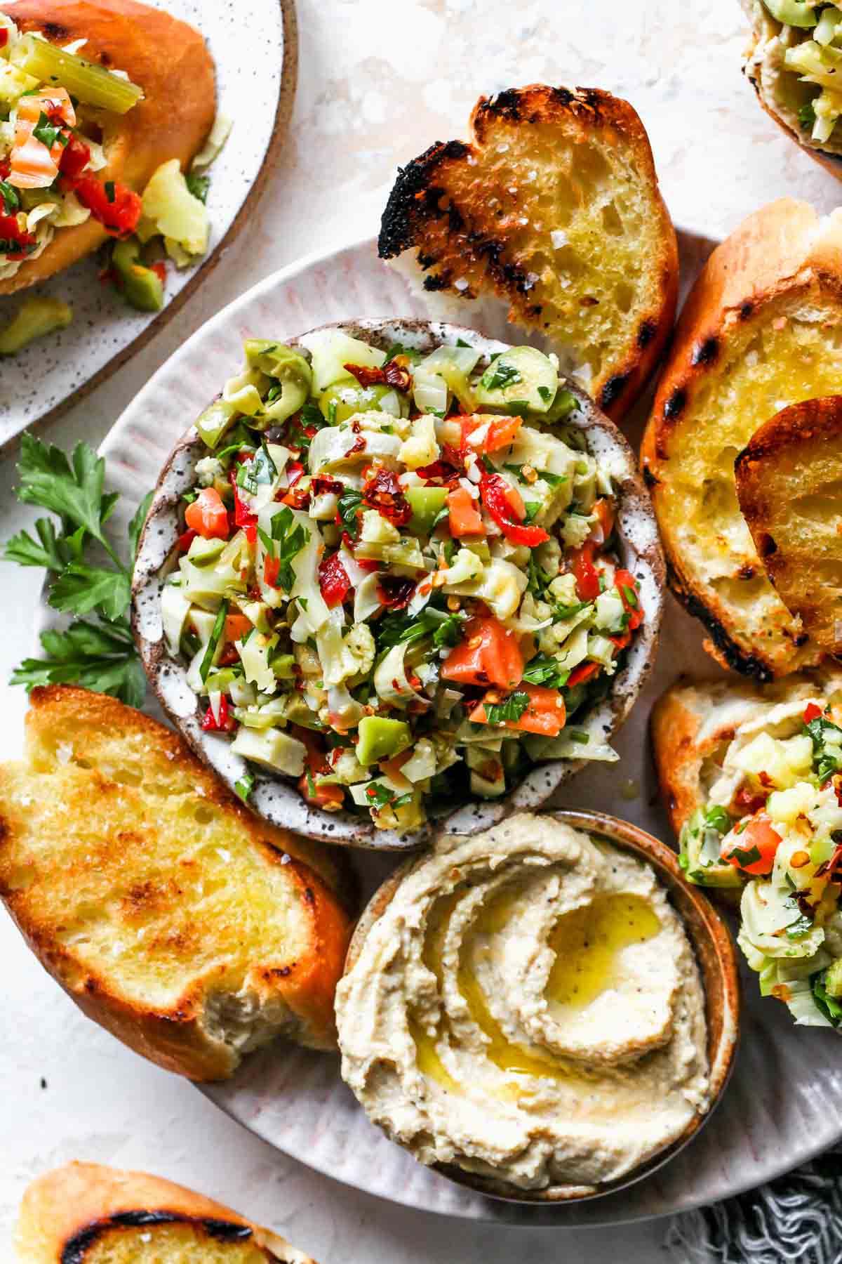 Artichoke salad in a bowl on a platter of toasted bread and hummus