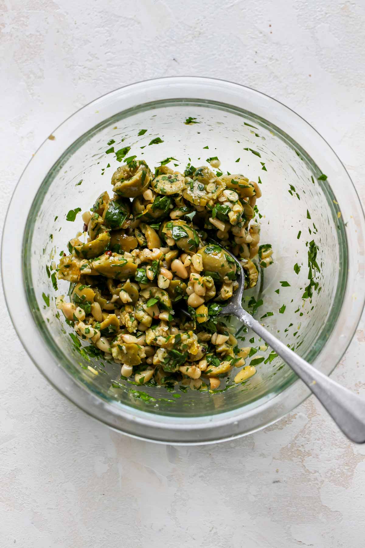 Olives, pine nuts, parsley, and lemon zest being mixed in a bowl