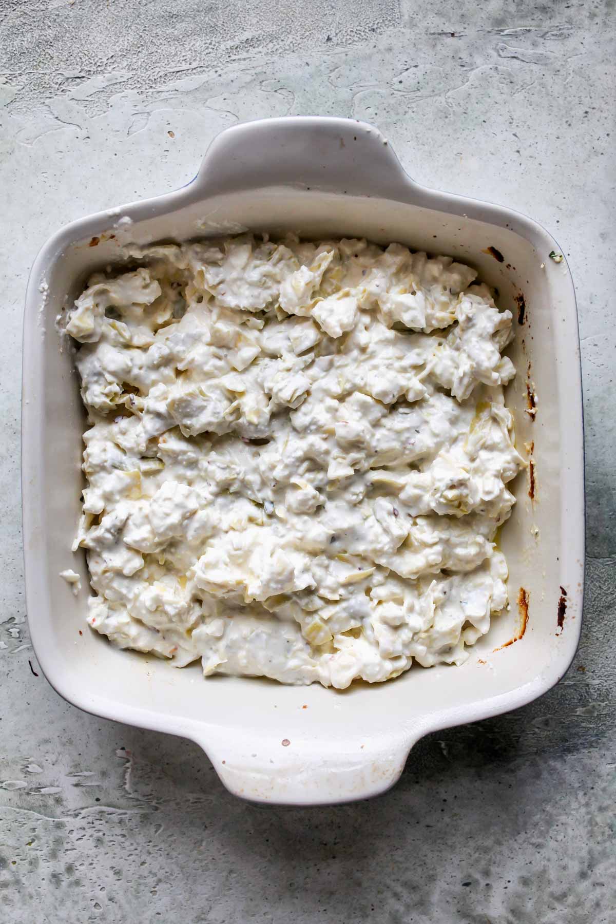 Feta, artichokes, mayo, and mozzarella mixture being transferred to a baking dish