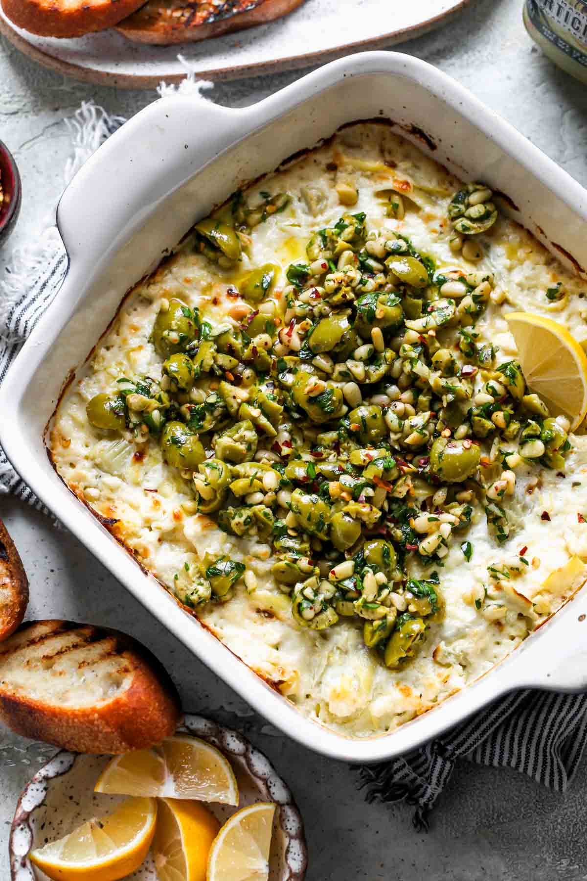Baked feta and olive dip in a baking dish served with crostini on the side