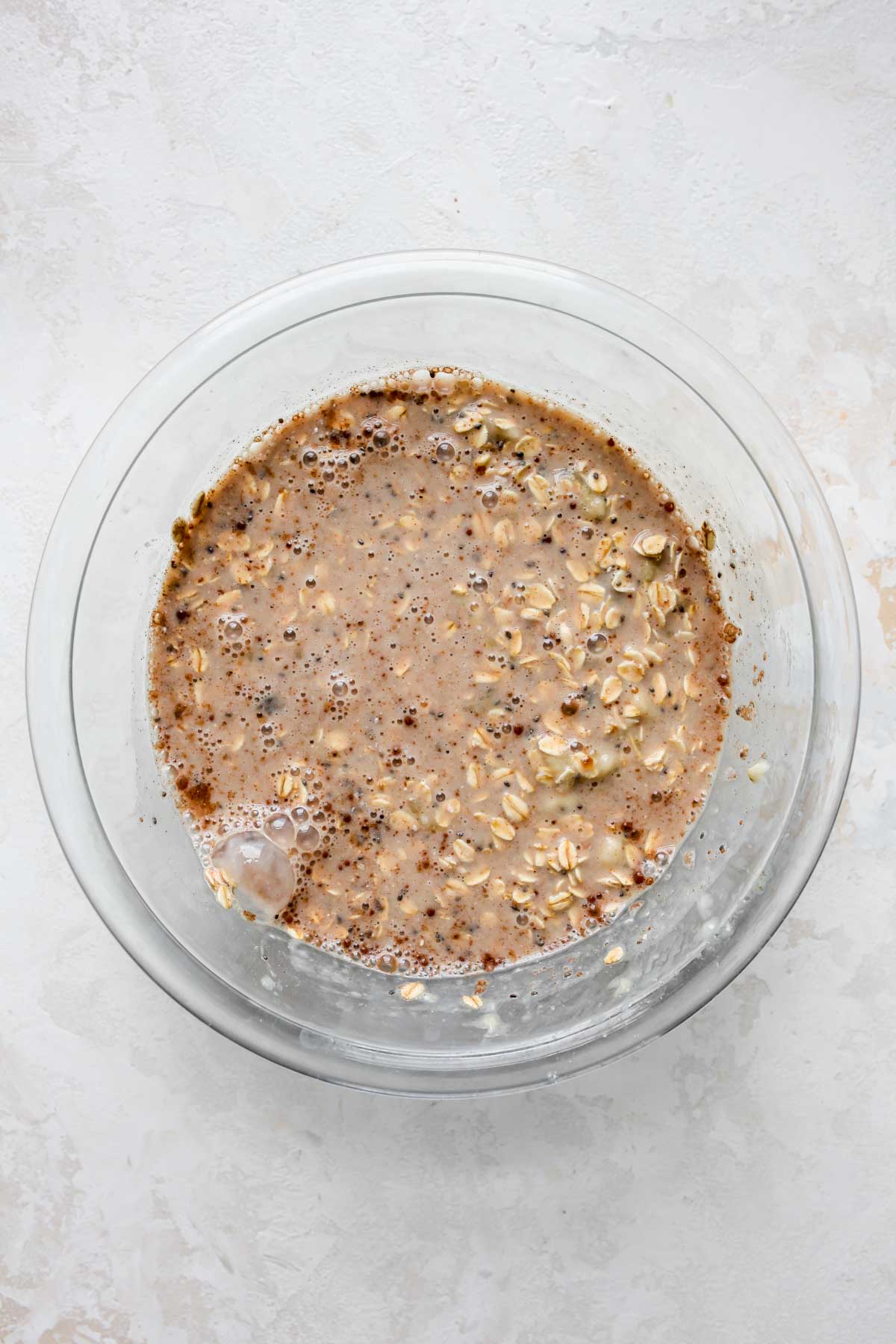 Oats, milk, spices, and dates being mixed in a clear mixing bowl