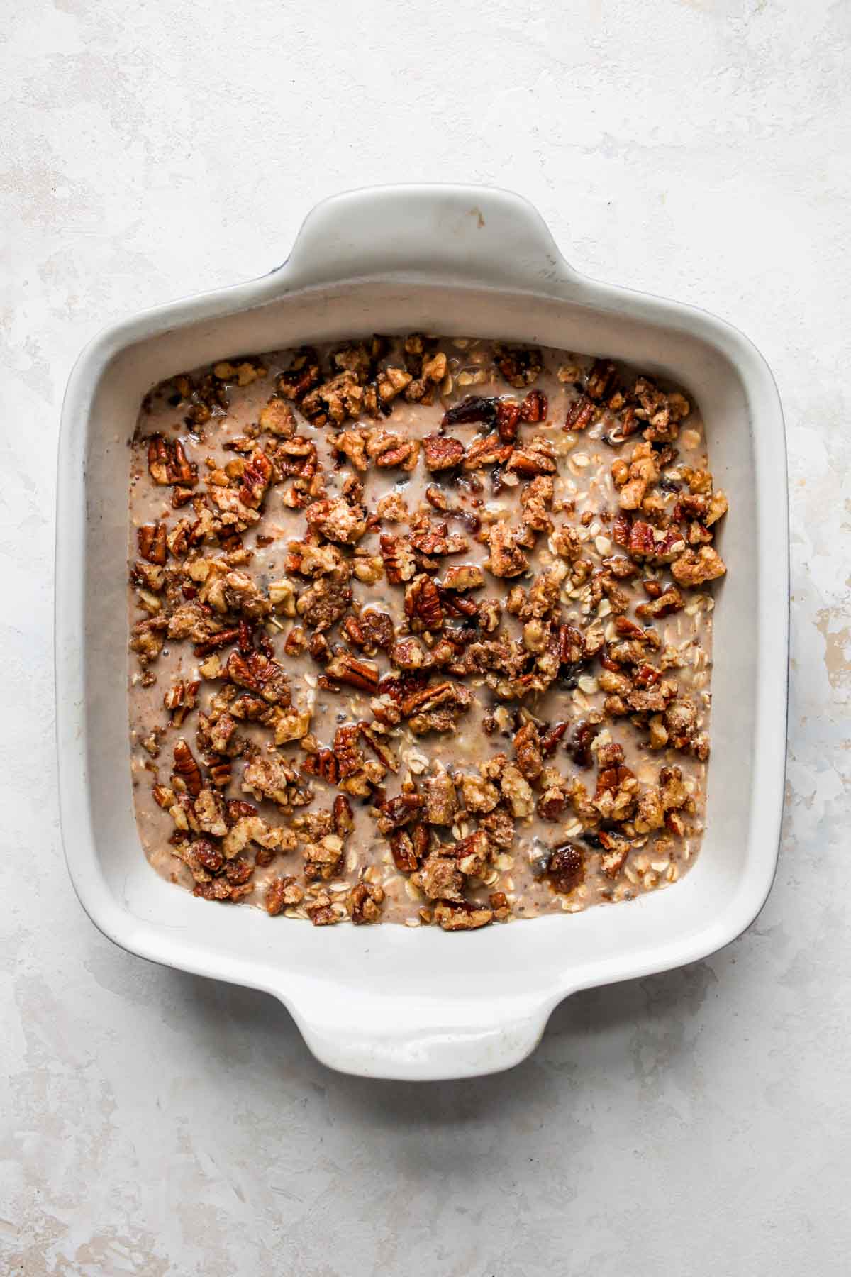 Oat mixture being poured into a baking dish and topped with pecan crumble