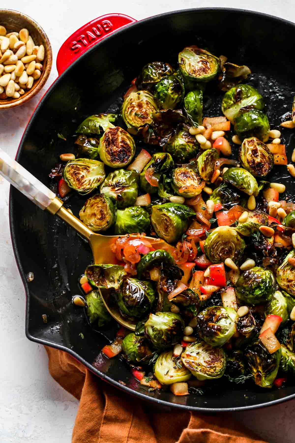 Cider-glazed Brussels sprouts styled in a red and black cast iron skillet with a gold serving spoon resting on the left side.