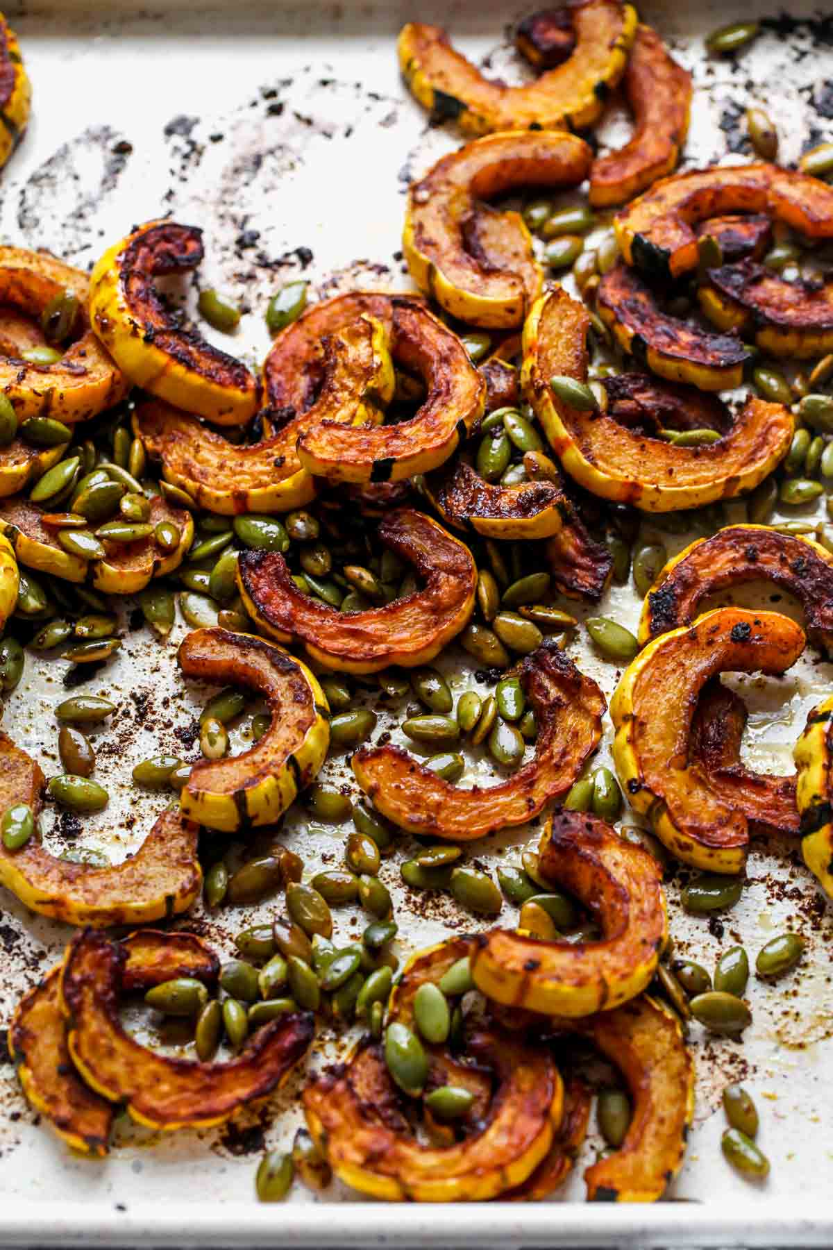Slices of roasted squash and pumpkin seeds roasted on a baking sheet
