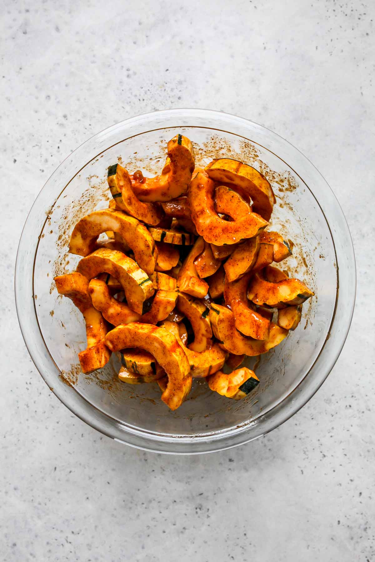 Slices of squash being tossed with oil and spices in a bowl
