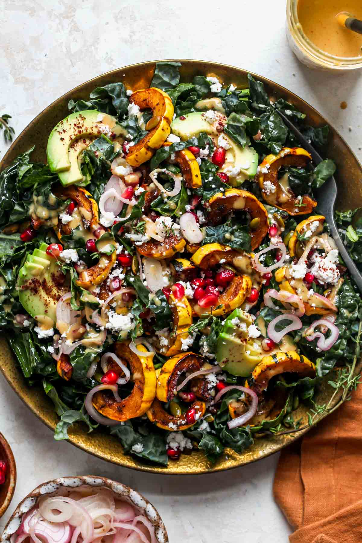 Kale salad with delicata squash, avocado, pomegranate, and pumpkin seeds on a gold plate