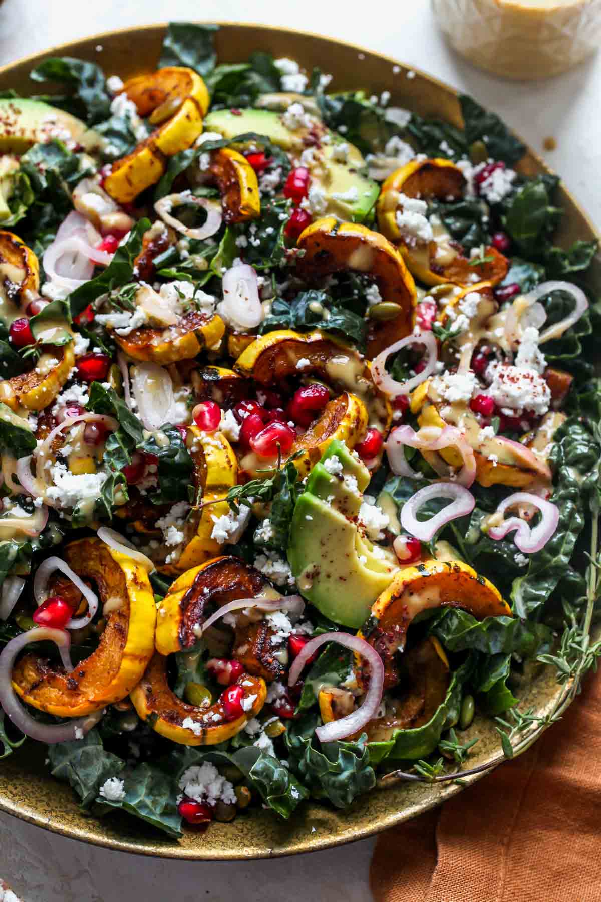 Kale and squash salad with pomegranate, avocado, and pickled shallots on a serving platter