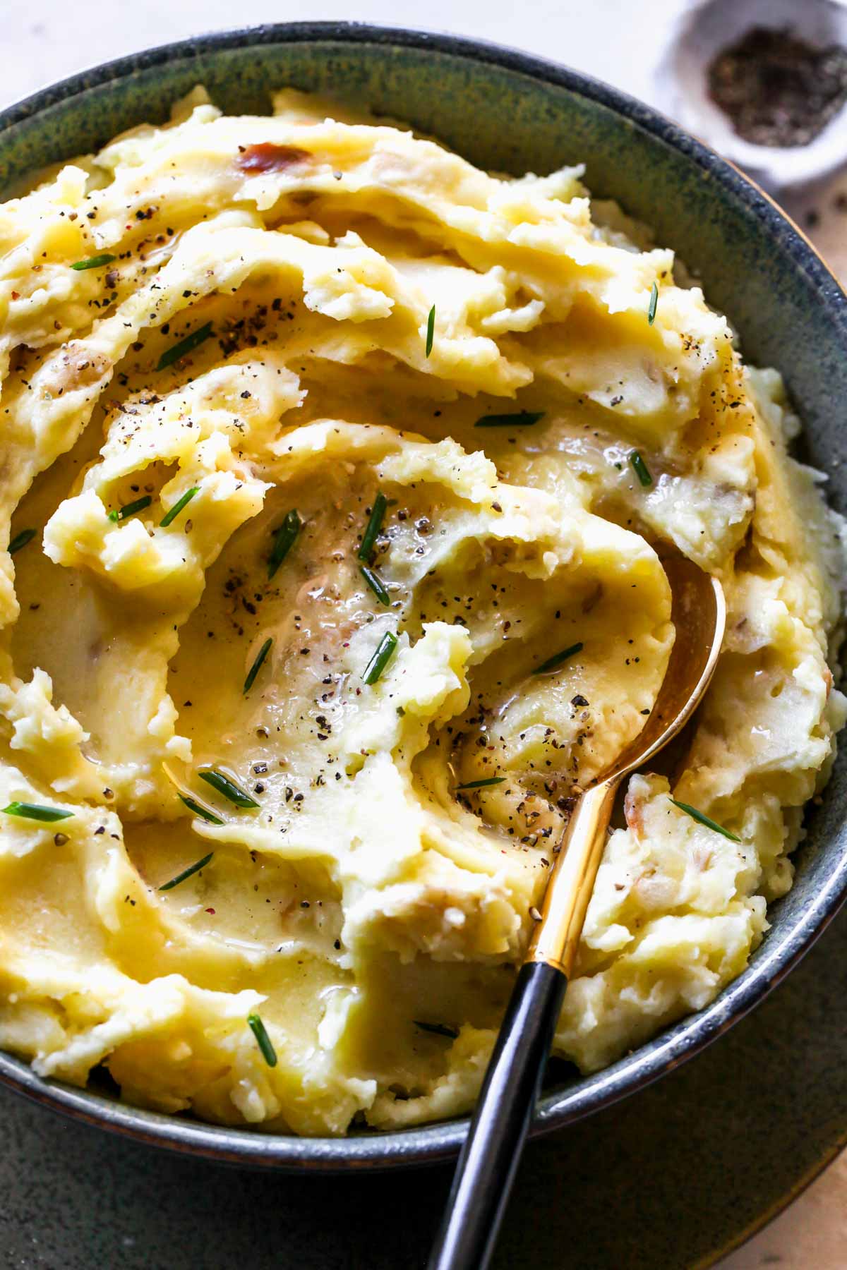 Mashed potatoes in a black and blue bowl topped with chives and cracked black pepper.