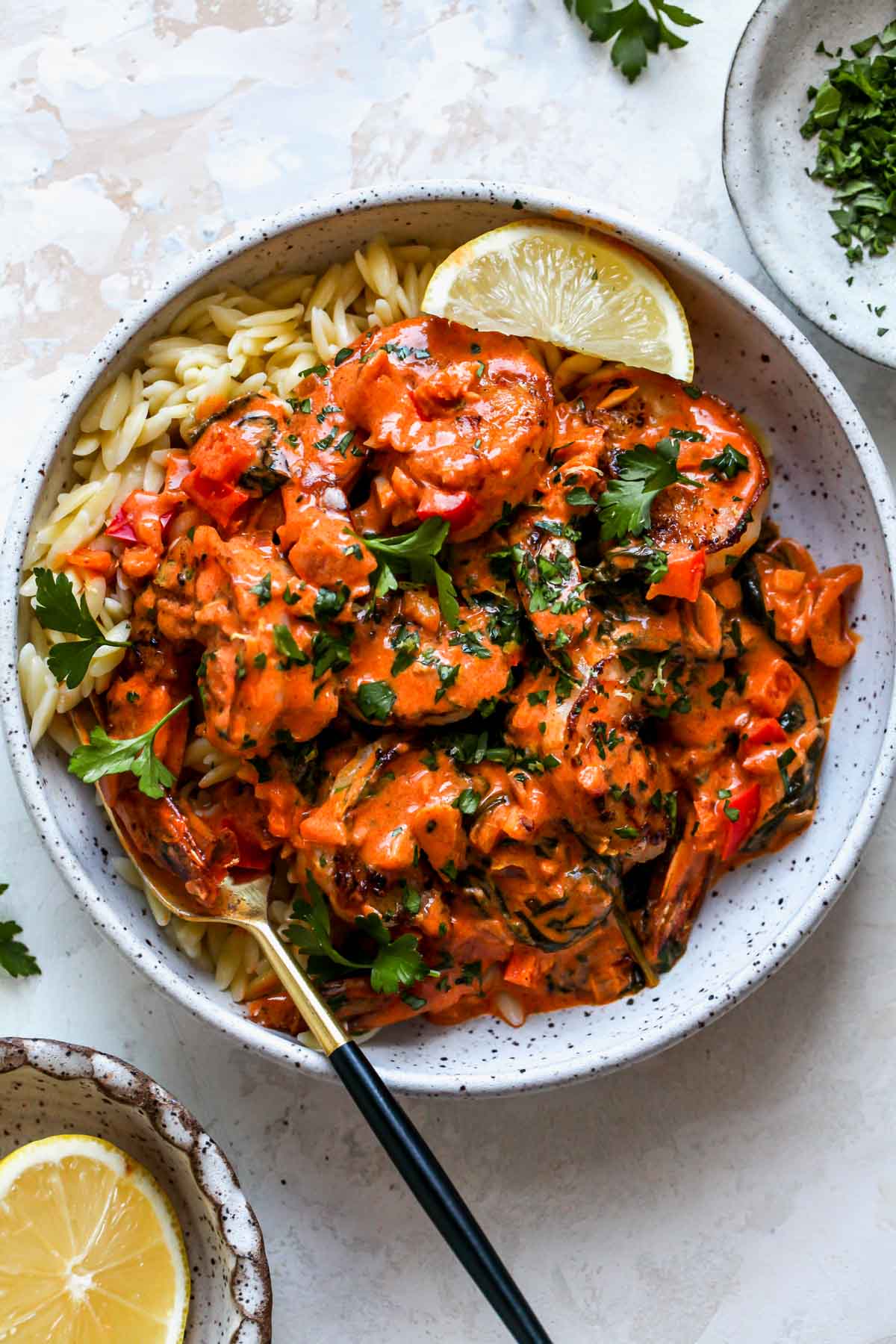 White bowl filled with orzo and creamy shrimp with a fork on the left side