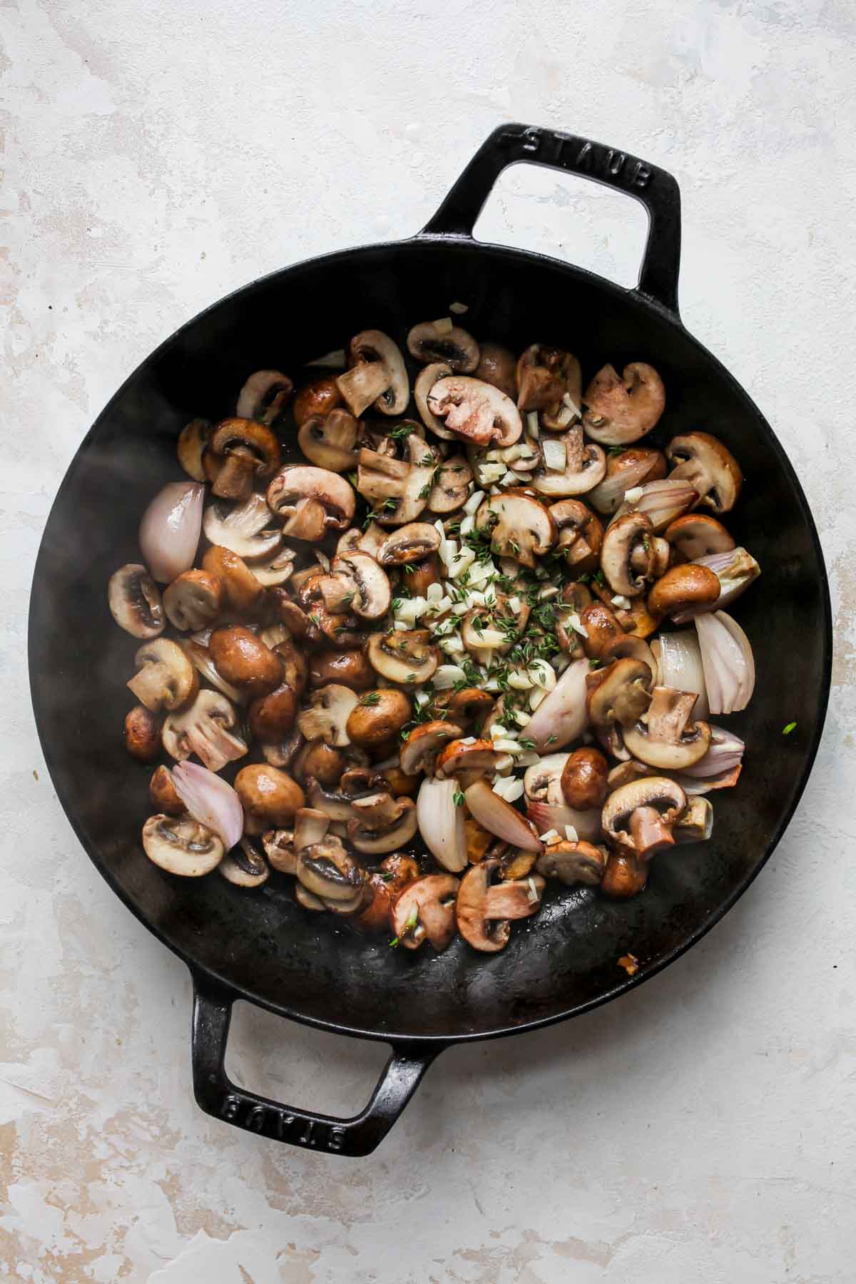 baby bellas, shallots, garlic, and thyme sautéing in a black skillet