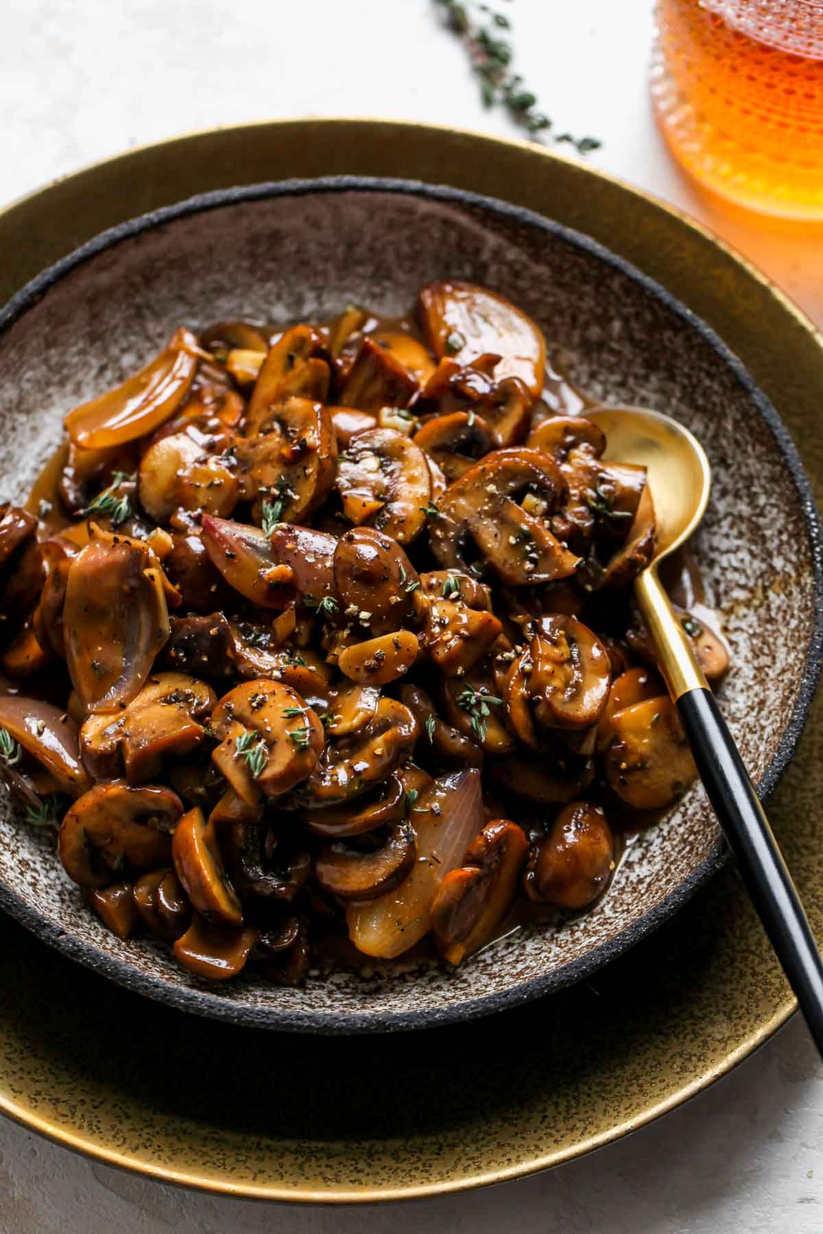 Bowl of mushrooms in marsala sauce with a gold serving spoon resting on the right side.