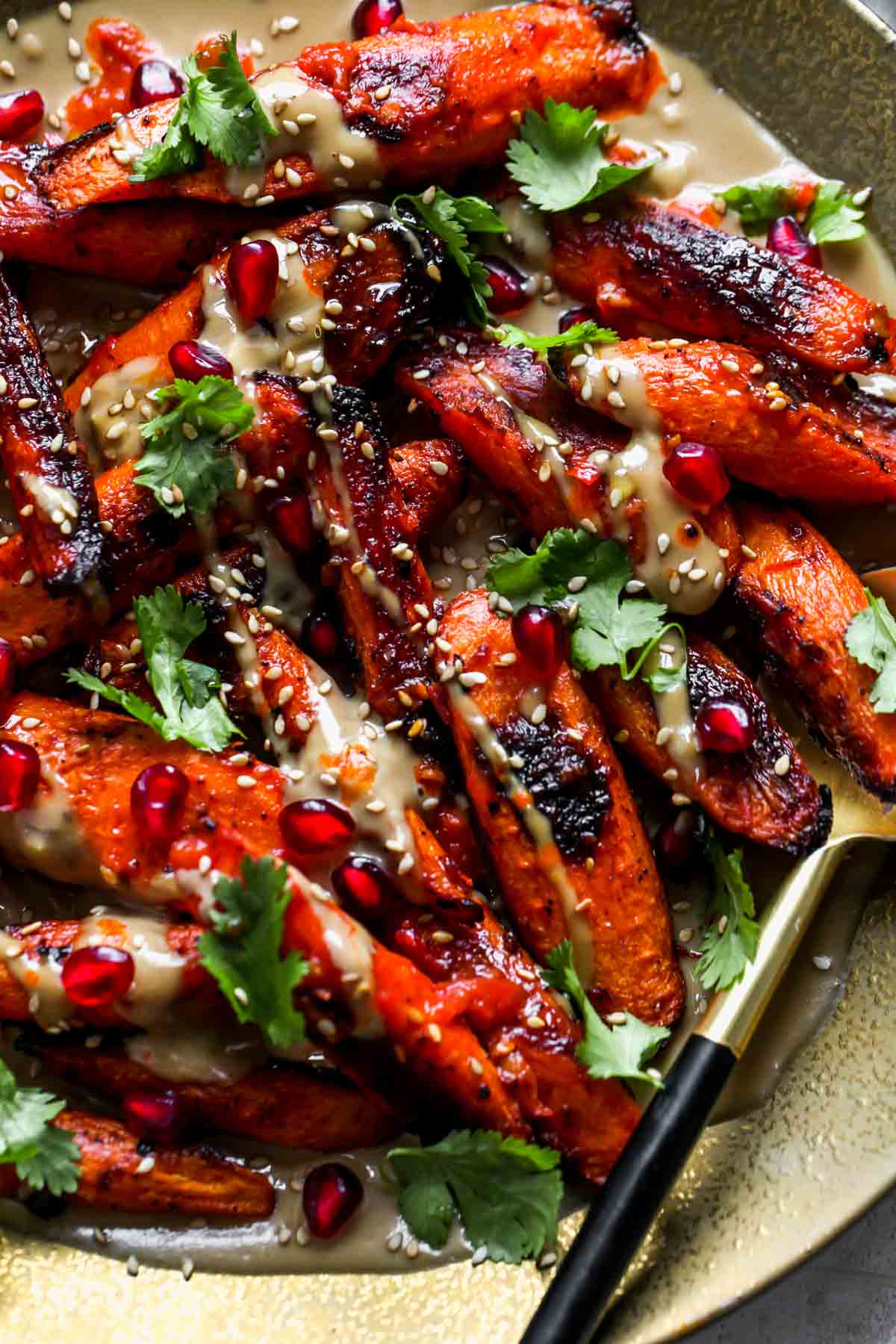 Roasted carrots with tahini sauce, cilantro, and pomegranate on a gold serving platter