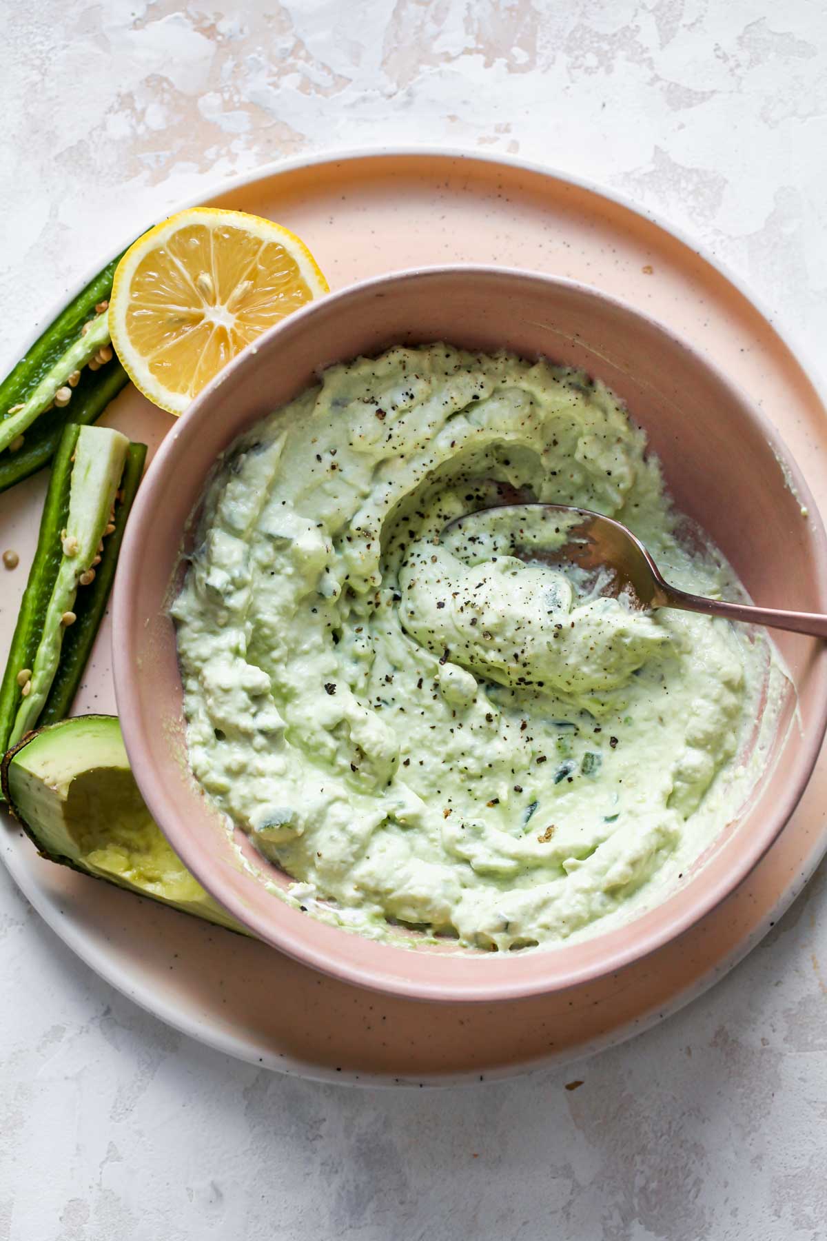 Avocado crema in a pink bowl with a spoon resting on the side.