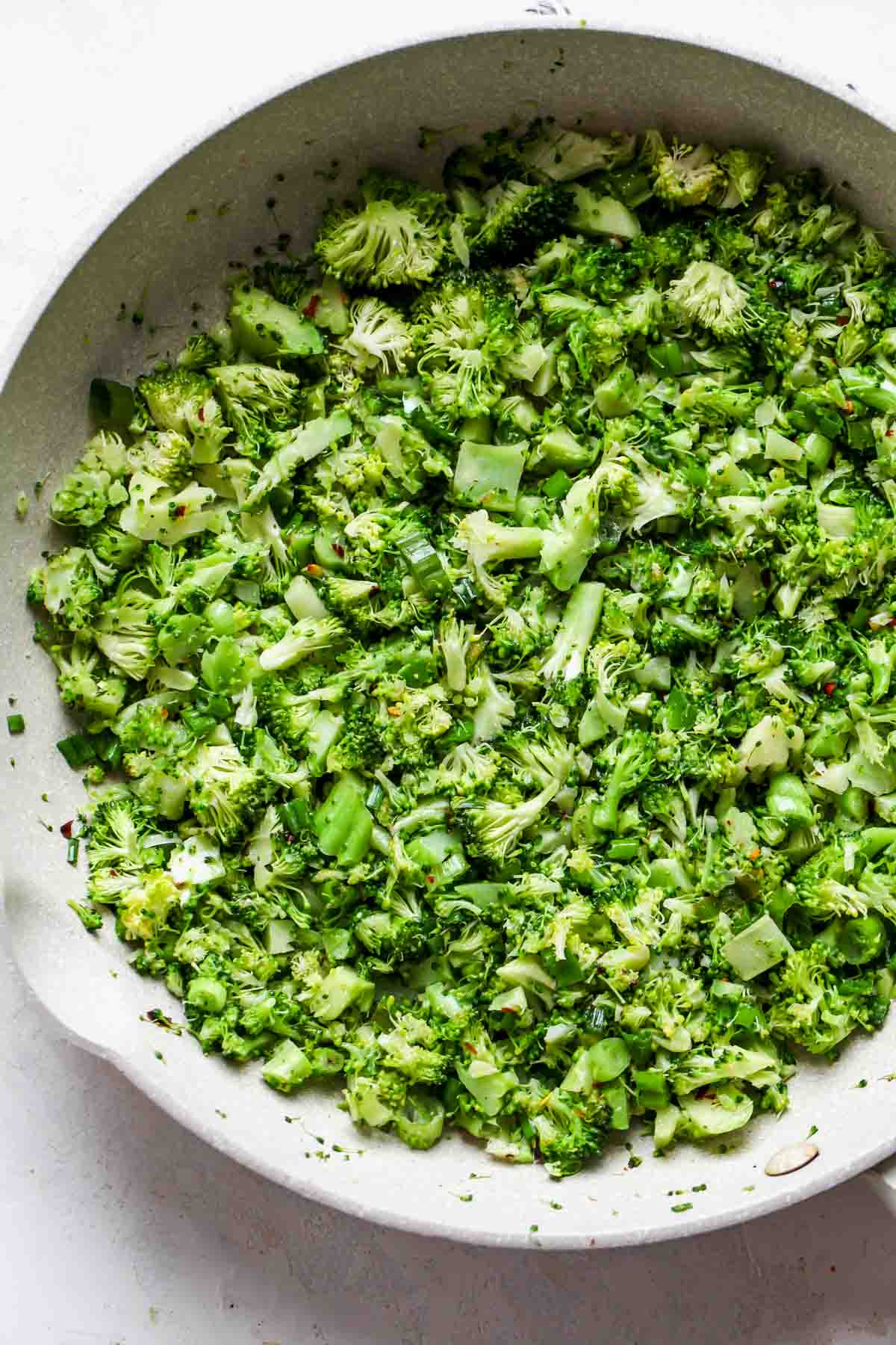 Broccoli, scallions, and chili flakes sautéing in a white skillet