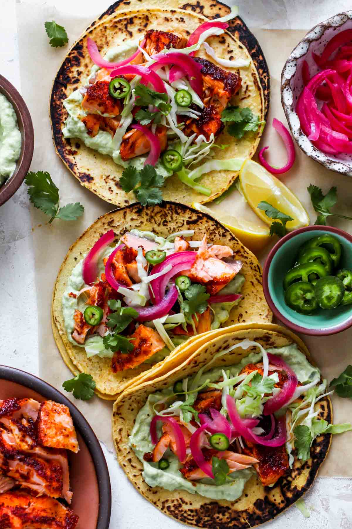 Three assembled salmon tacos on a piece of parchment paper.