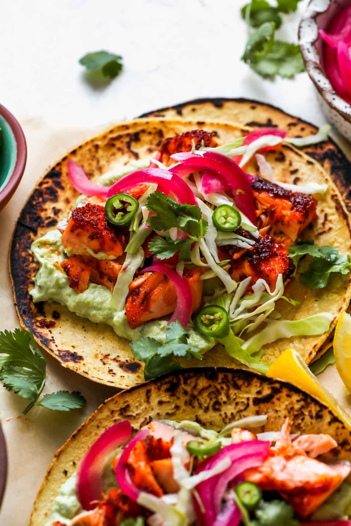 Salmon tacos topped with red onion, slaw, and avocado.