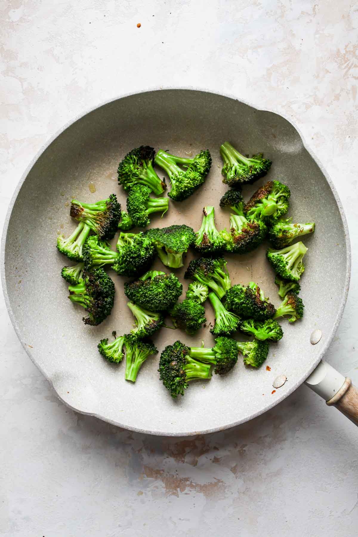 Broccoli florets being sautéed in a white skillet