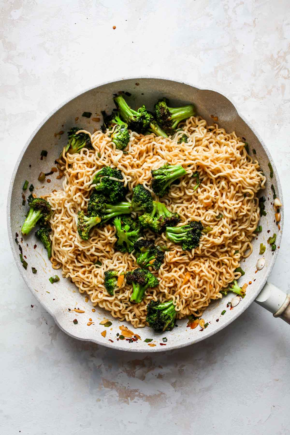Ramen noodles being added to a skillet of broccoli and aromatics