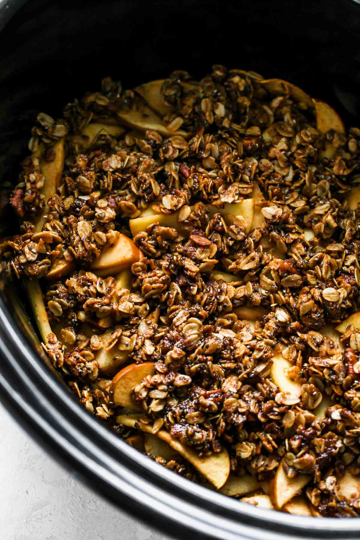 A slow cooker pot filled with sliced apples and oat crumble mixture