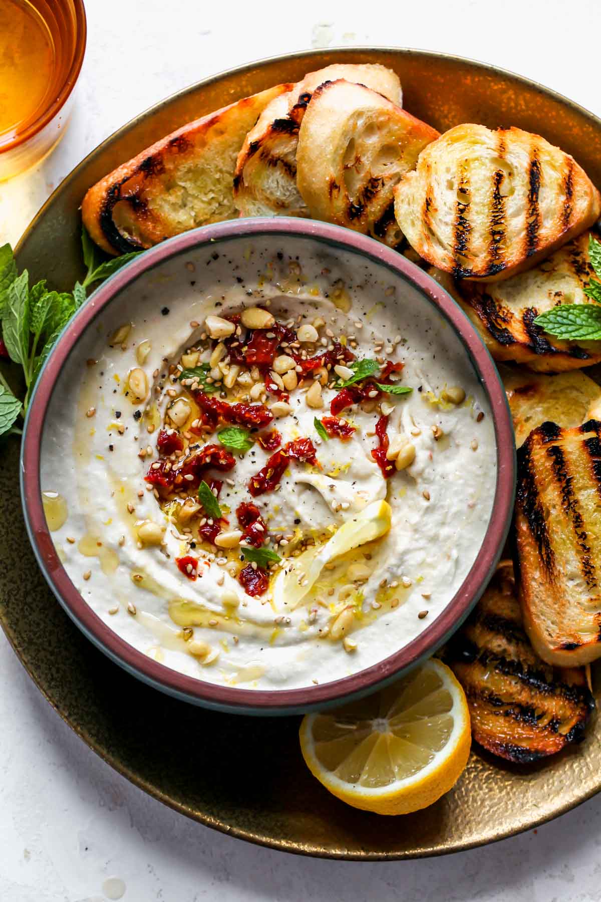 White bean dip in a bowl topped with sun-dried tomatoes and pine nuts