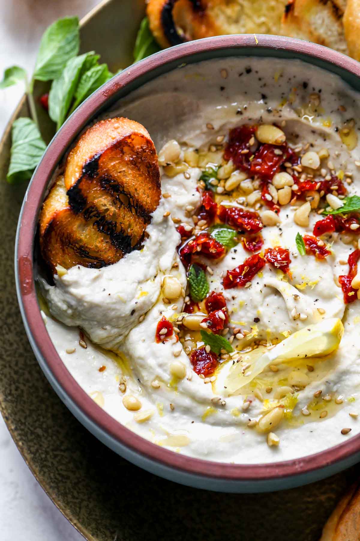 A piece of grilled bread being dipped into a bowl of artichoke dip