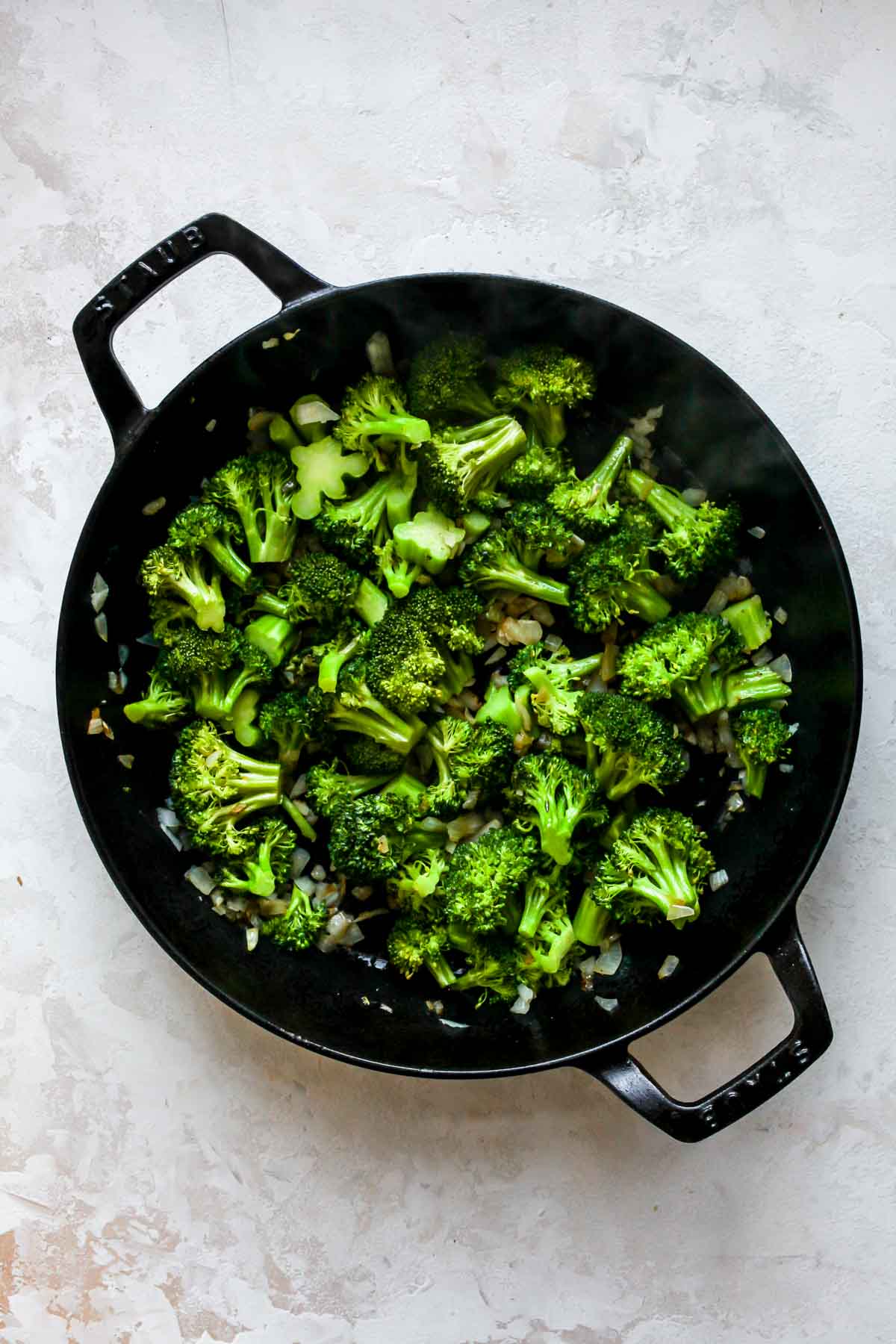 Broccoli florets and onion being sautéed in a skillet