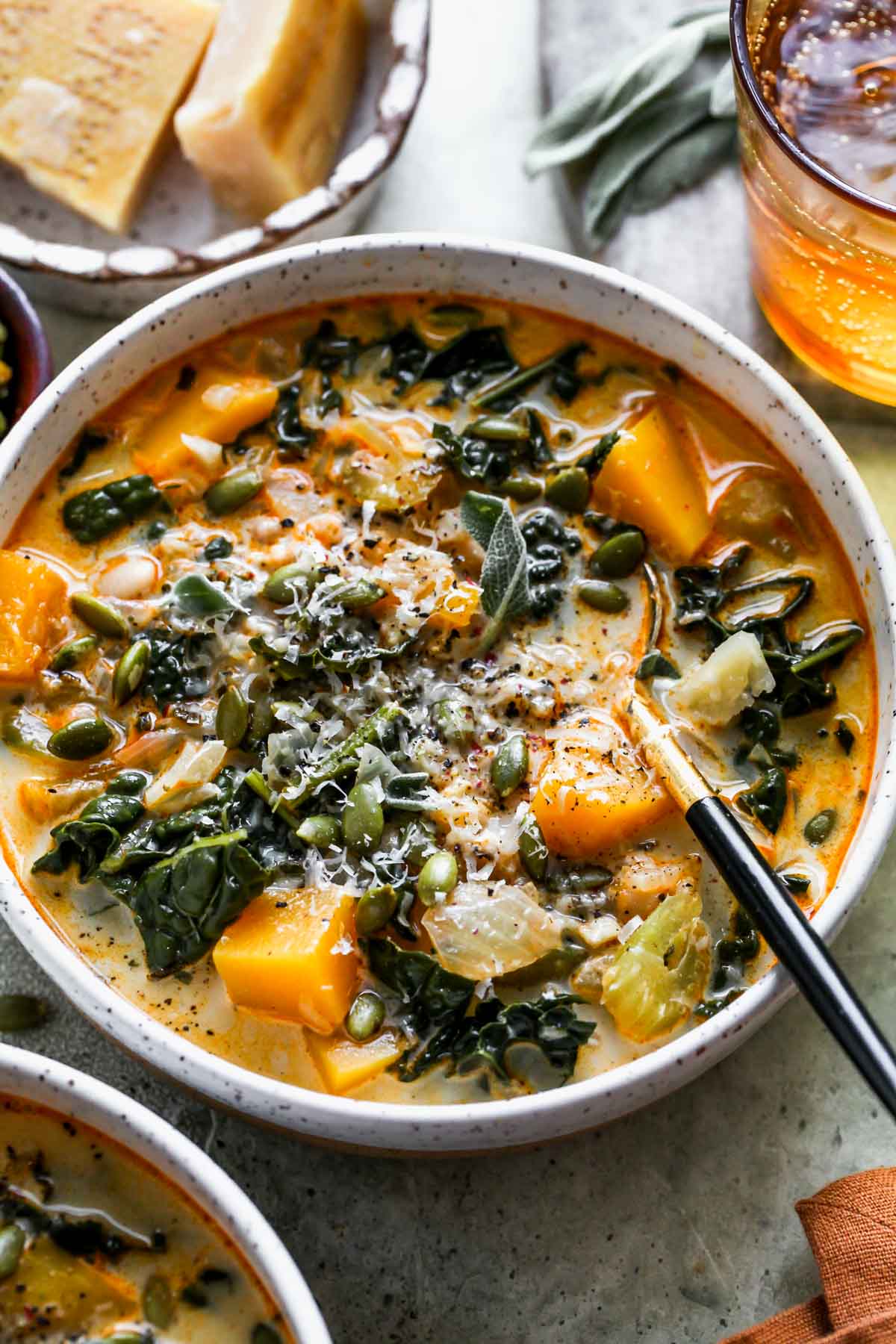 Squash, kale, and white bean soup in a white bowl with a spoon resting on the right side.