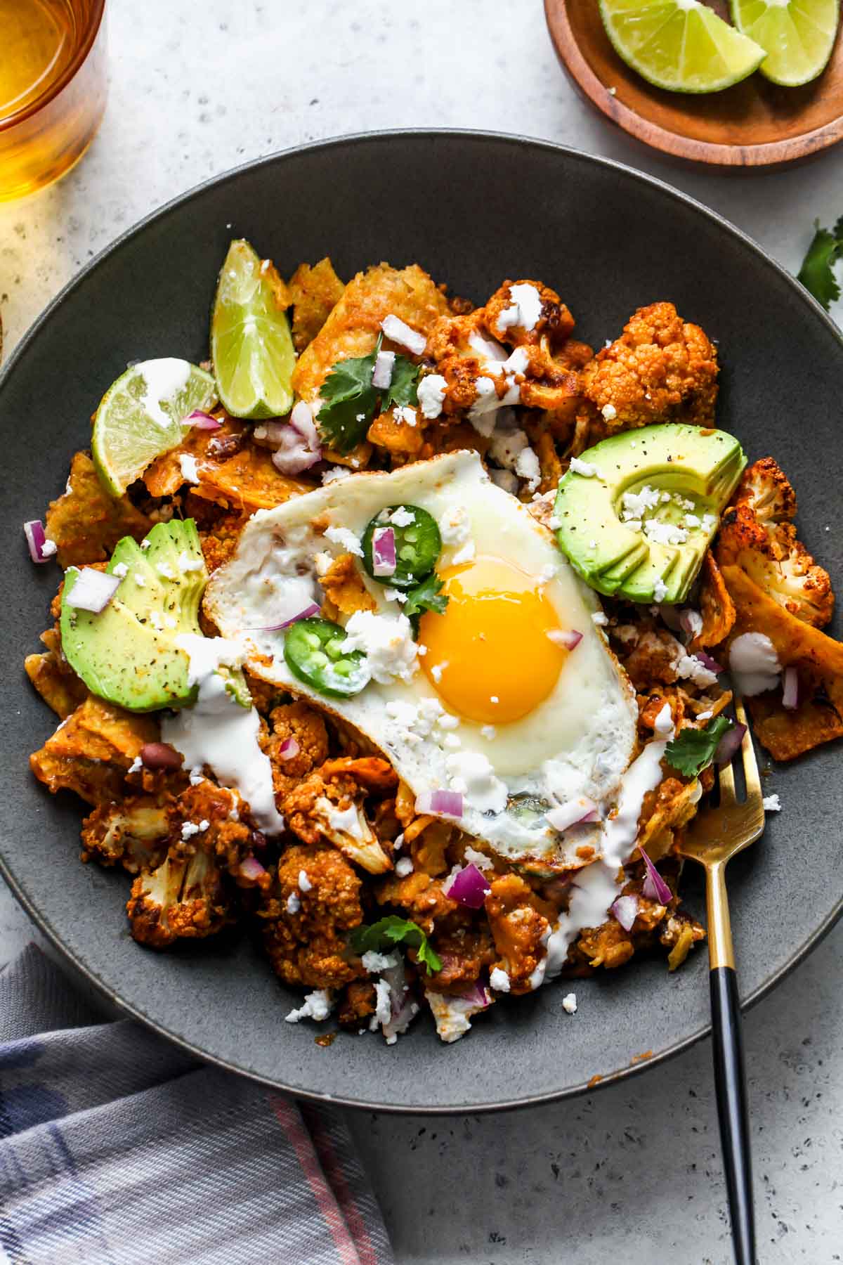 A black bowl filled with roasted cauliflower, tortilla chips, salsa, roja, and fried eggs