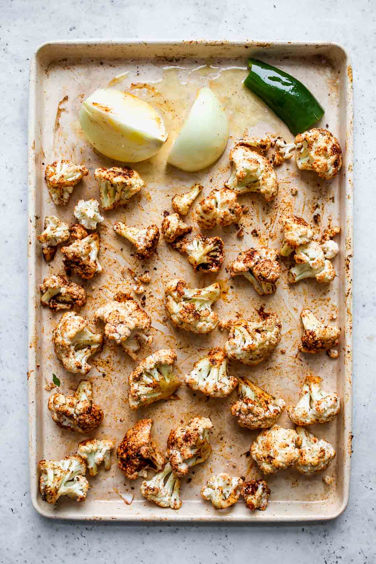 Cauliflower and onion being roasted on a white baking sheet