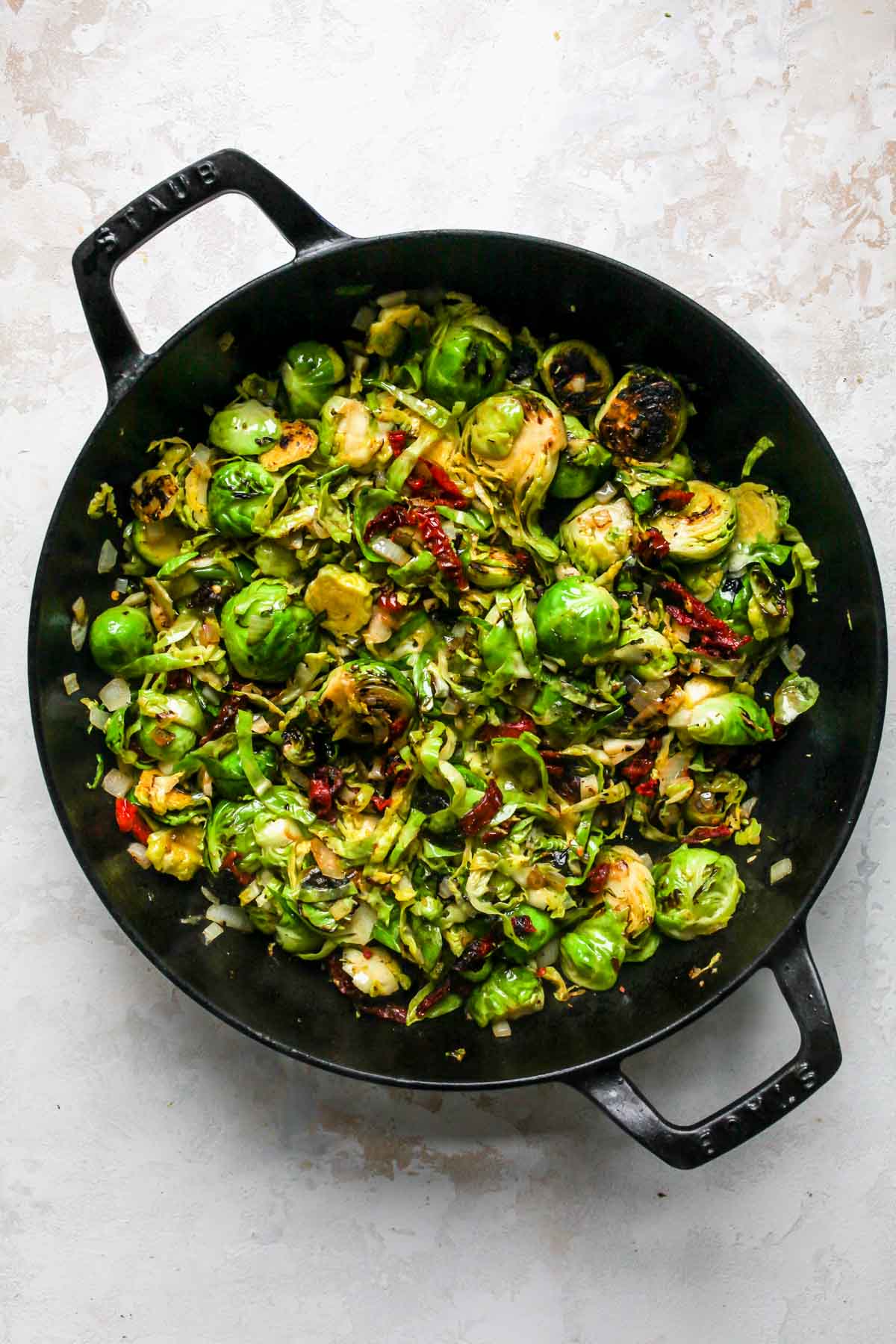 Brussels sprouts, sun-dried tomatoes, and onions sautéing in a skillet