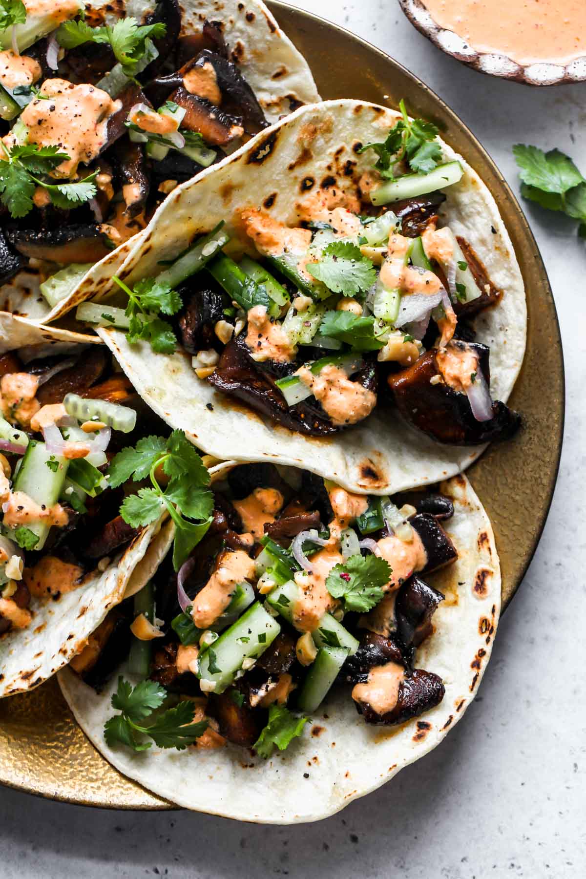 Korean tacos styled on a gold plate with a bowl of kimchi cream on the side