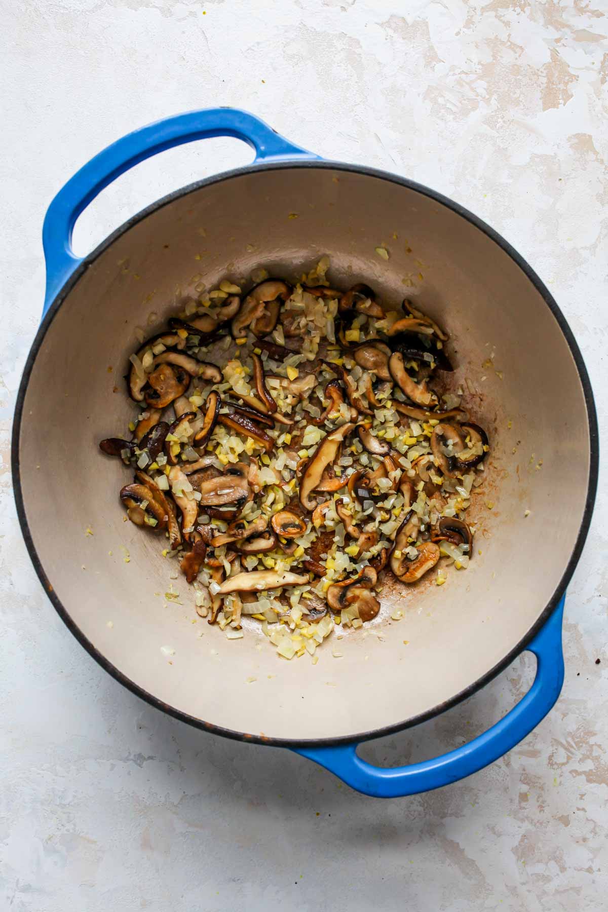 Shiitake mushrooms, ginger, garlic, and scallions sautéing in a large blue Dutch oven.