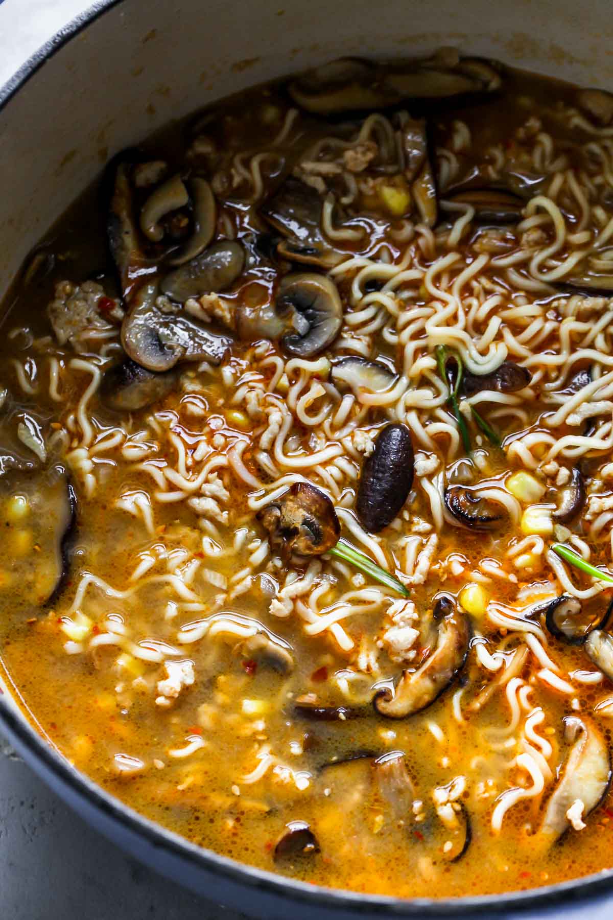 Noodles and broth simmering in a pot of mushrooms and aromatics.