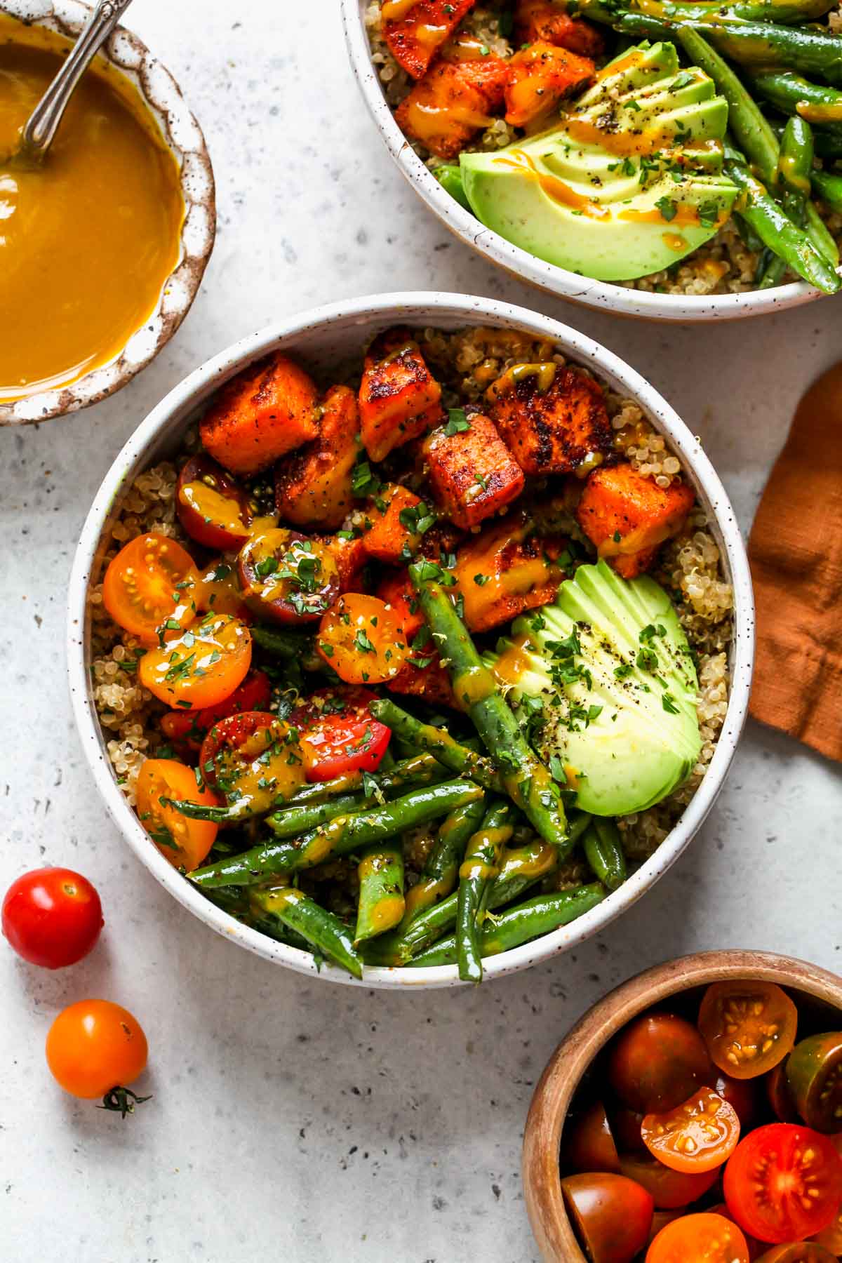 Roasted sweet potato bowls topped with green beans, tomatoes, and avocado slices. A drizzle of honey mustard sauce overtop.