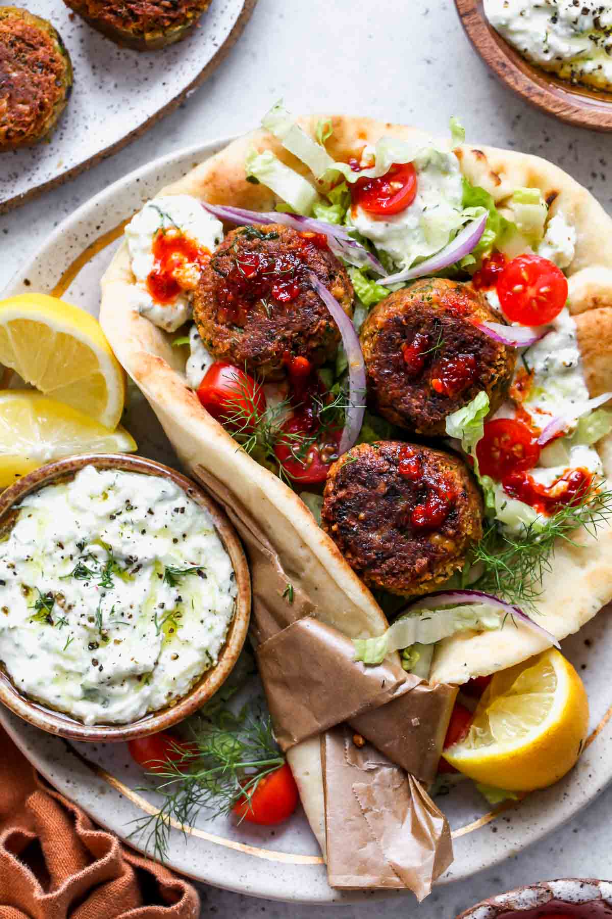 Falafel gyros with feta tzatziki, lettuce, tomato, and red onion assembled on a plate