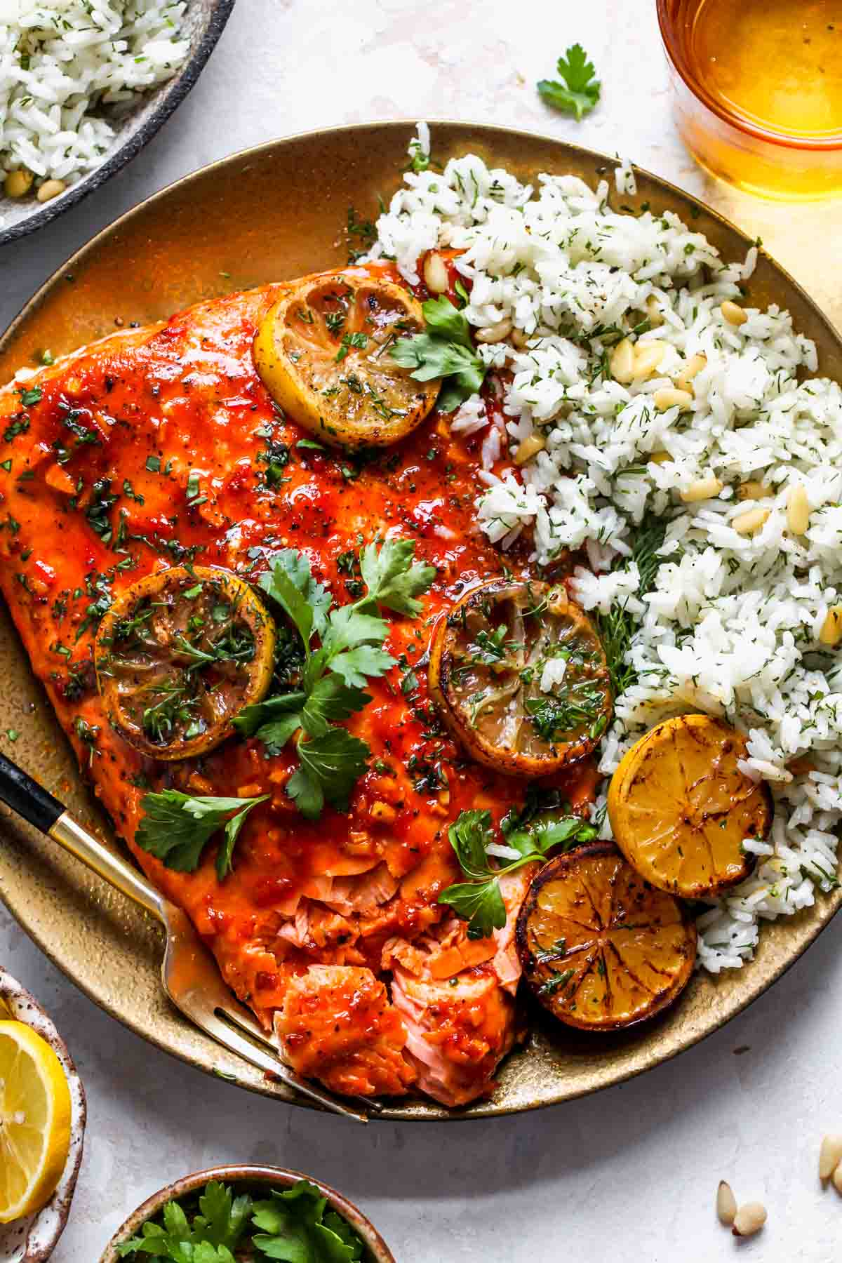 Harissa baked salmon fillet on a gold plate with dill rice and lemon slices