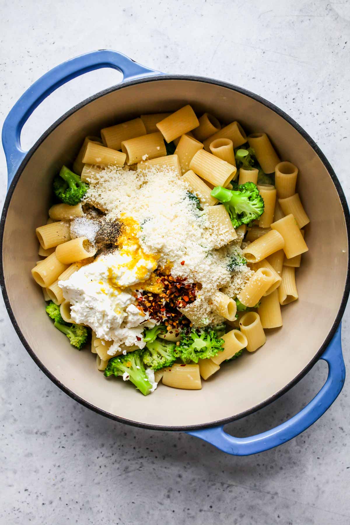 Ricotta, parmesan, and lemon being added to a pot of cooked rigatoni and broccoli