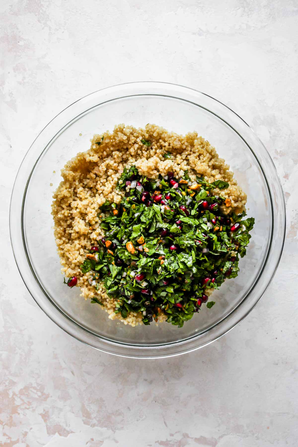 Herb mixture being tossed with cooked quinoa in a clear bowl