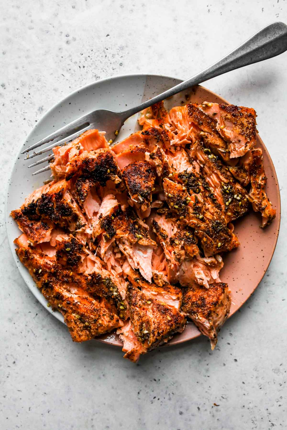 Cooked salmon fillet flaked into pieces on a plate
