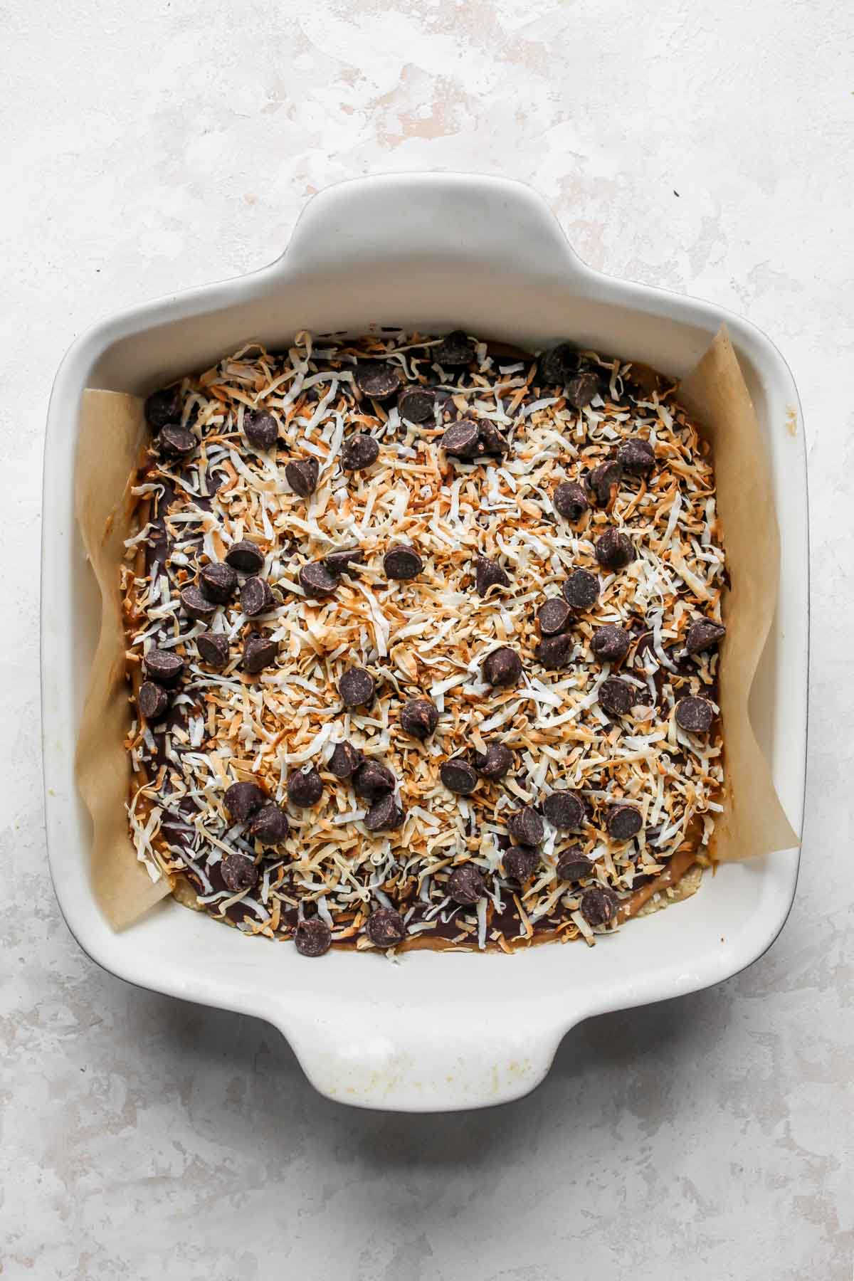 Toasted coconut and chocolate chips being layered on top of vegan bars
