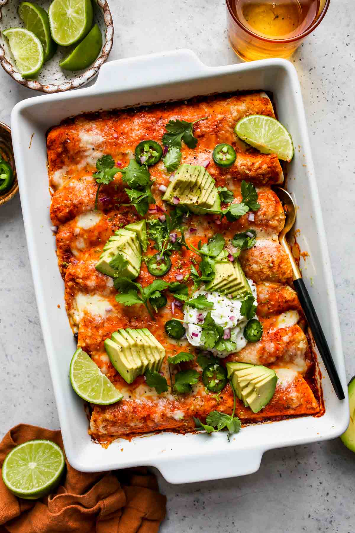 Veggie enchiladas baked in a white pan topped with avocado and cilantro