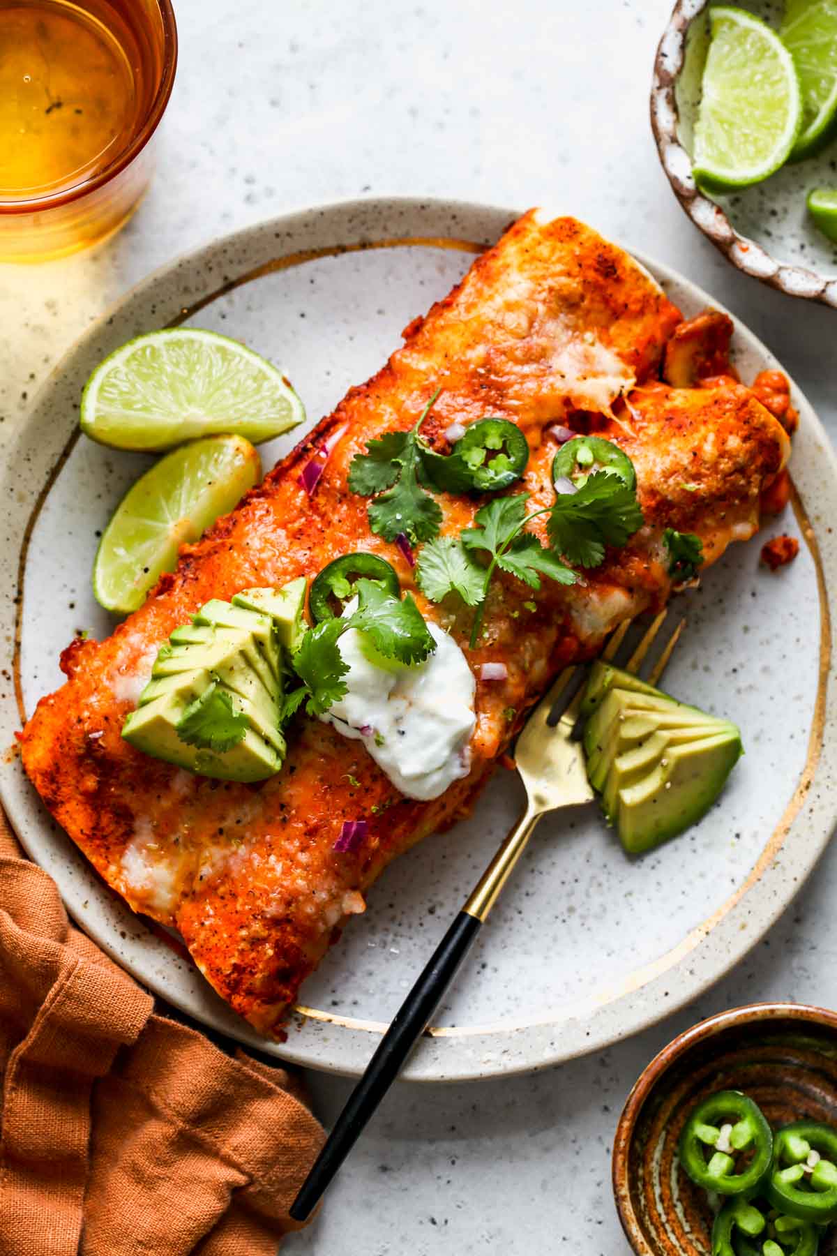 Two vegetarian enchiladas on a plate topped with yogurt and avocado