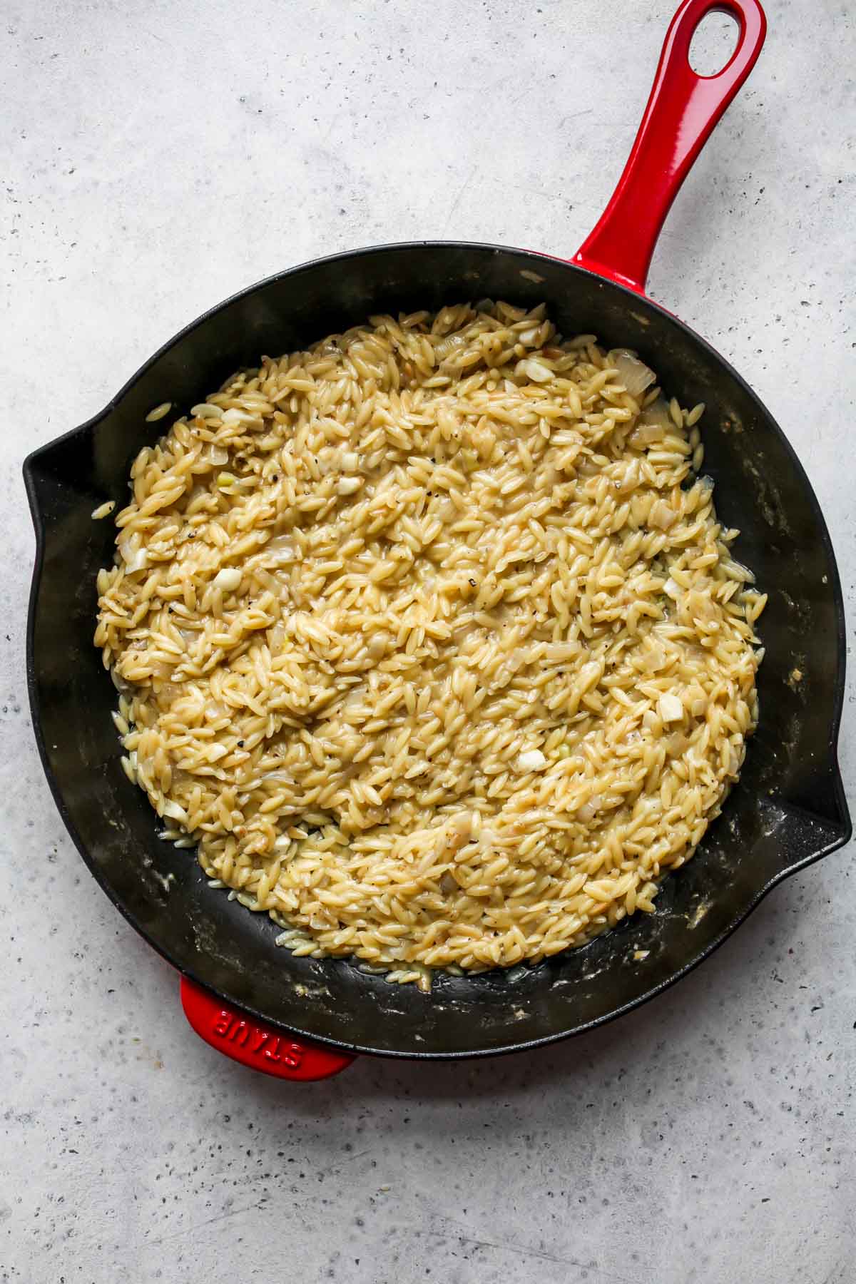 Cooked orzo pasta in a red and black pan.