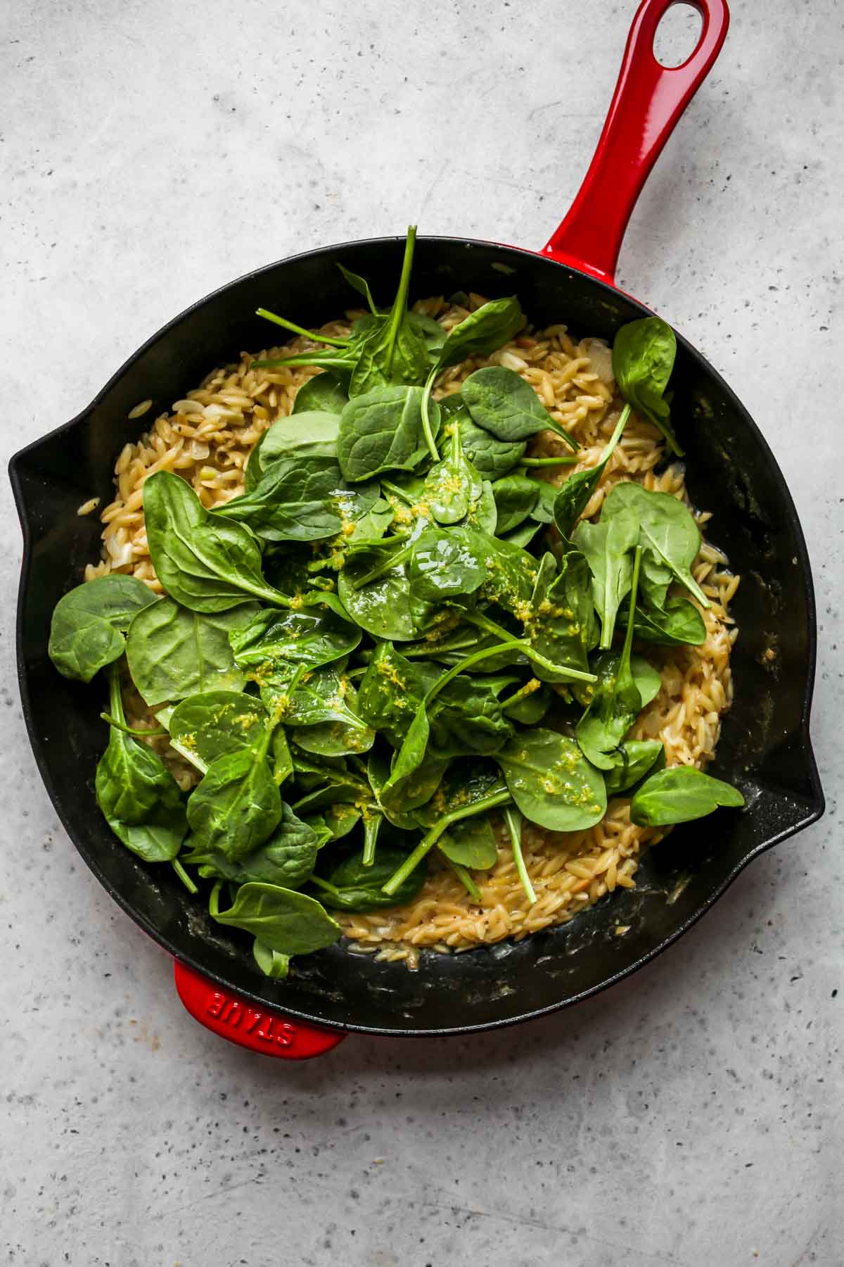 Spinach, lemon zest and juice being stirred into a pot of grains.