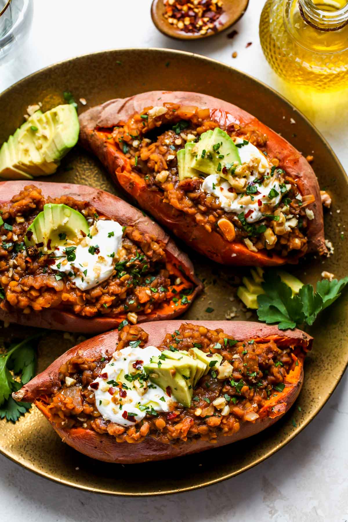 Lentil stuffed sweet potatoes arranged on a platter topped with avocado and parsley