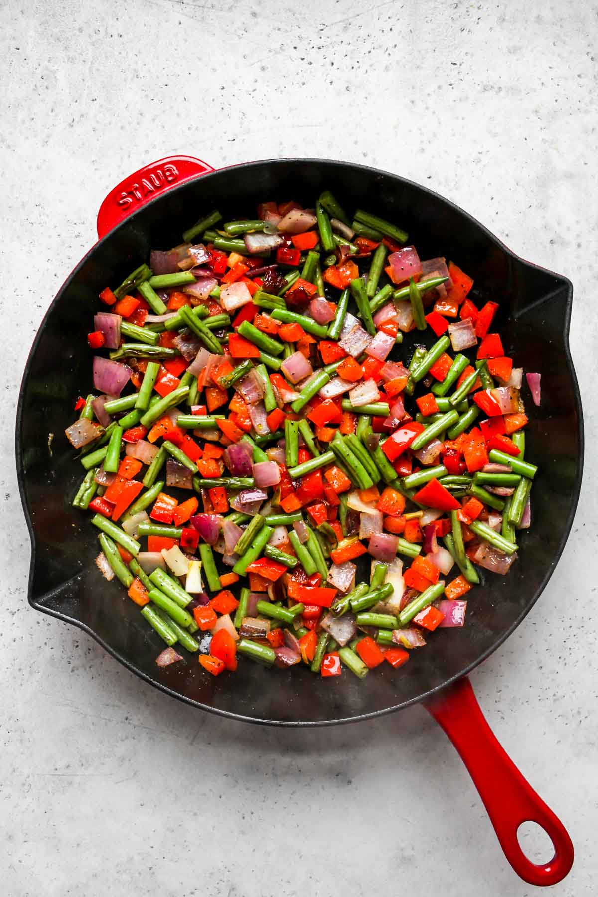Sauteed onion, bell pepper, and green beans in a skillet.