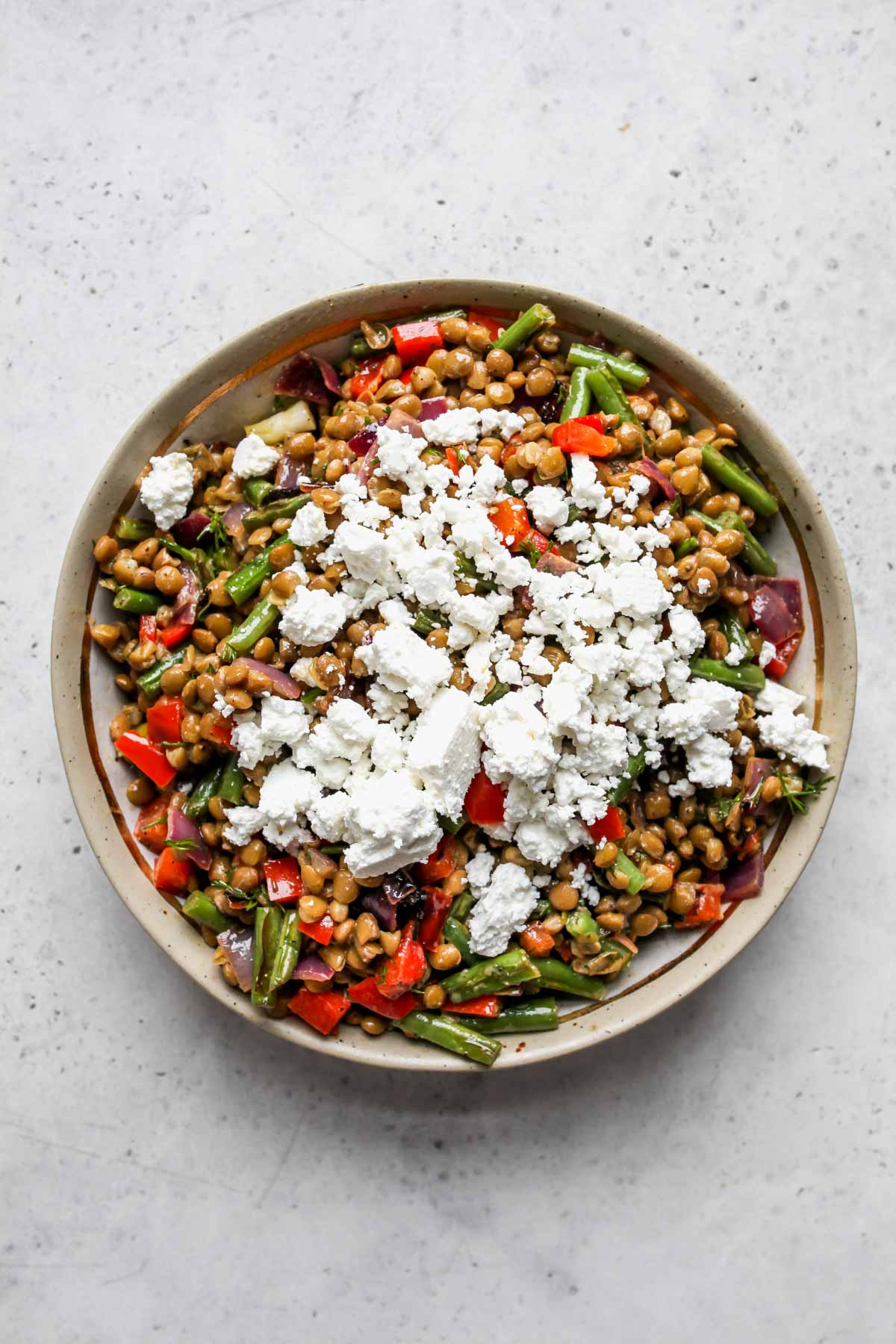 Feta cheese being added to a bowl of lentil salad.