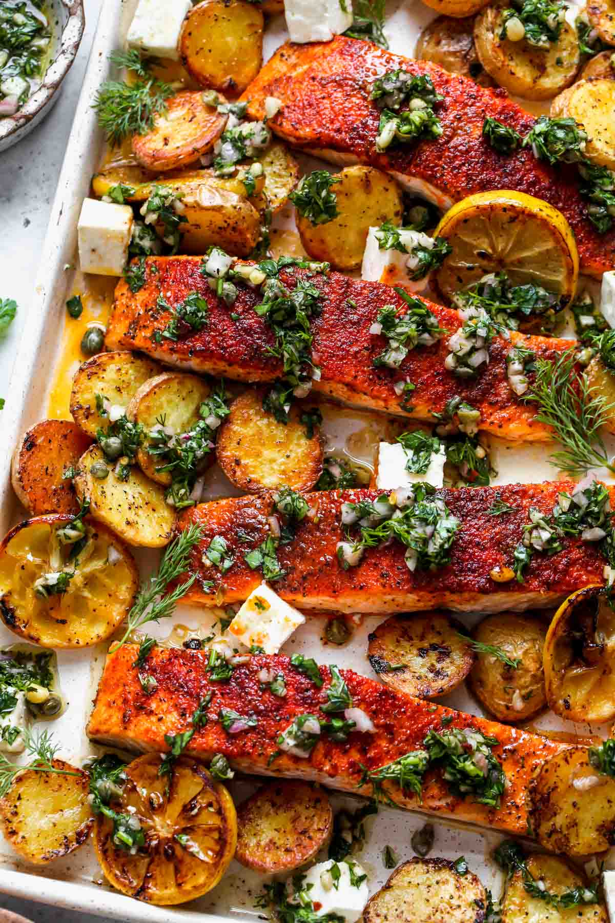 Sheet pan and salmon and potatoes roasted on a white baking sheet and topped with chimichurri