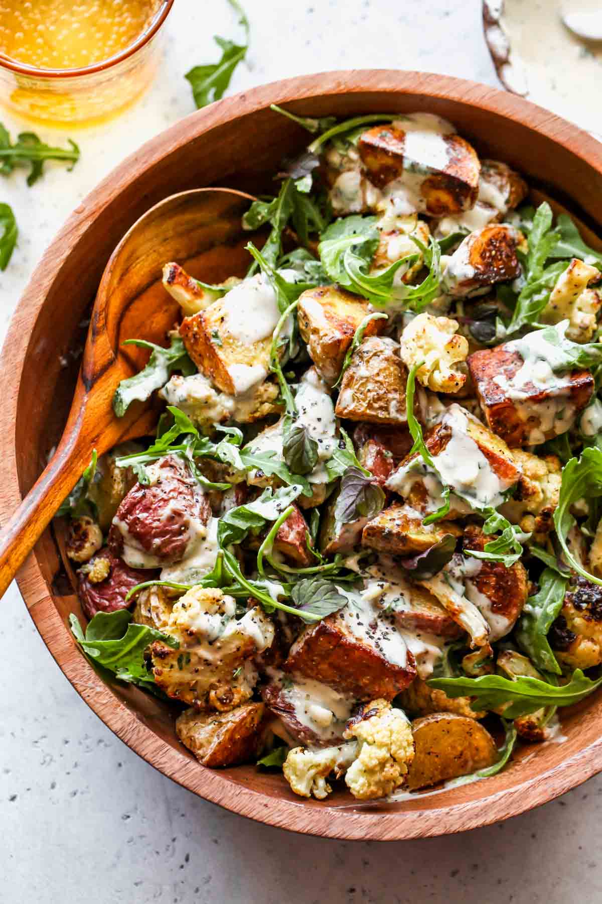 Roasted cauliflower, potatoes, arugula, and tahini dressing being mixed in a bowl.